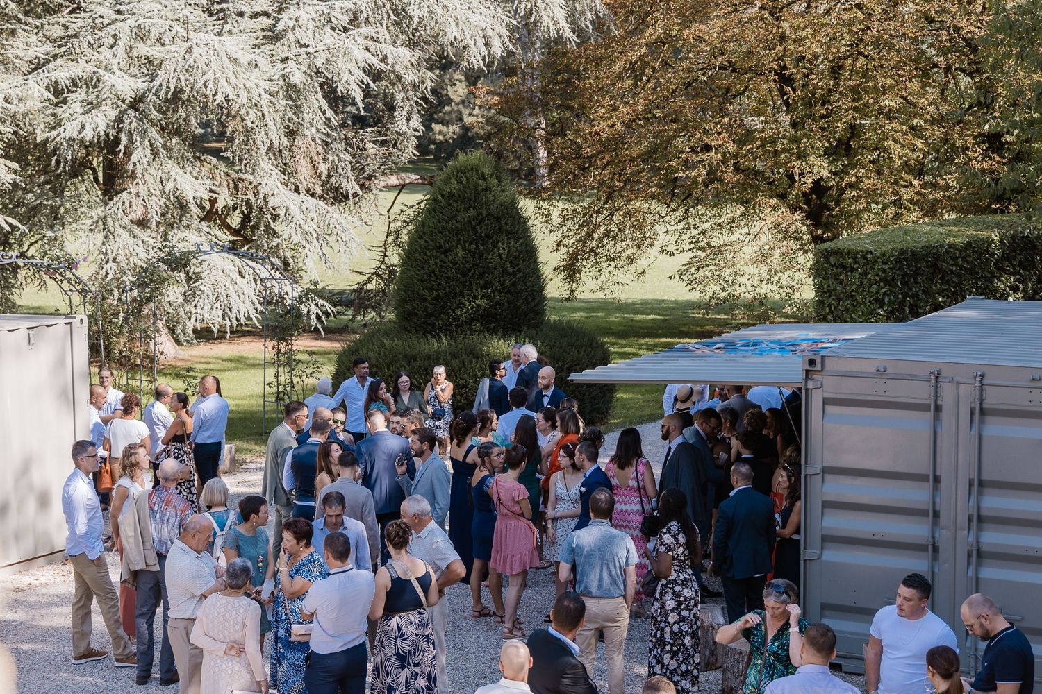 Elegant outdoor wedding cocktail reception with guests mingling in a sunlit garden near a historic venue.