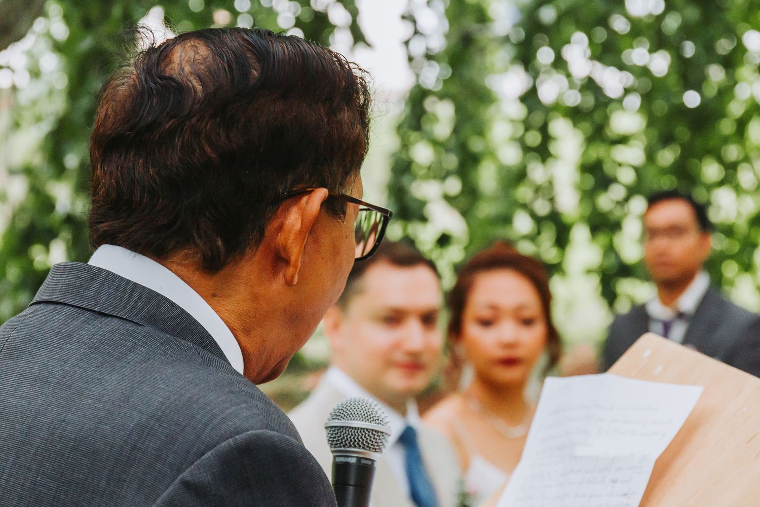 Wedding officiant reading from paper at podium with bride and groom listening in background.