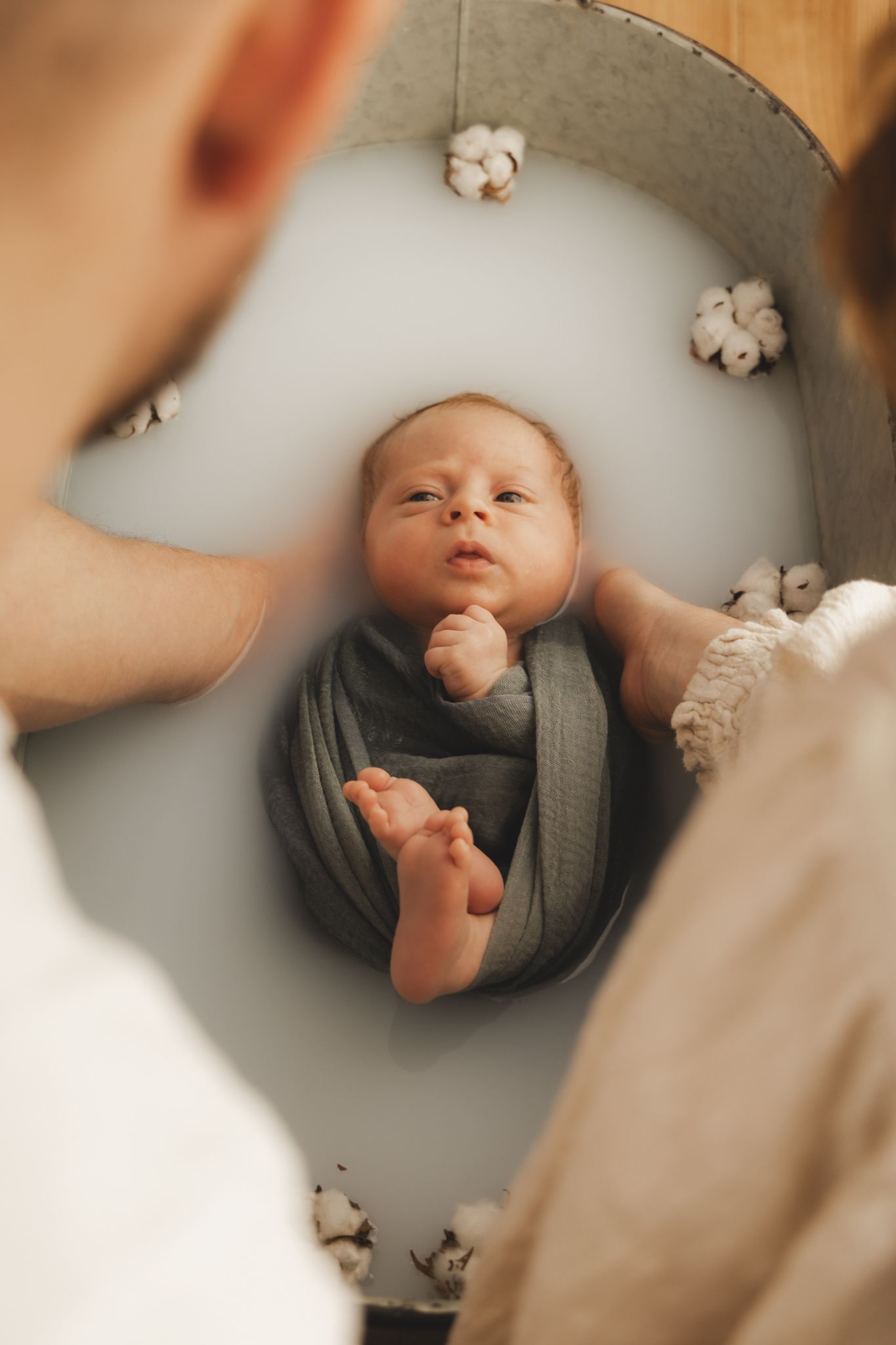 Séance photo nouveau-né en Isère : la douceur d'un bébé emmailloté dans un bain de lait décoré de fleurs de coton.