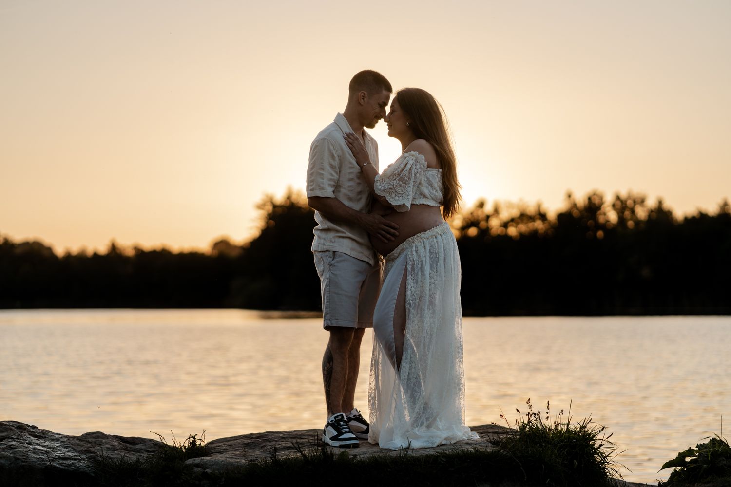 Couple sharing romantic moment standing on rocks by lake at golden sunset.