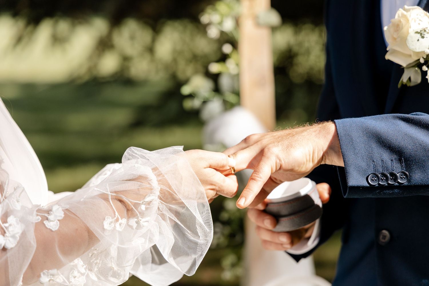 Groom gently places a wedding ring on the bride's finger during the outdoor ring exchange ceremony.
