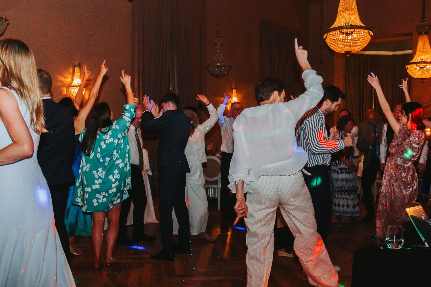 Wedding guests raising hands and dancing energetically on the dance floor at a reception party.