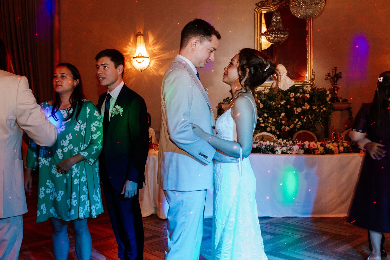 Bride and groom sharing romantic first dance under colorful lights at wedding reception.