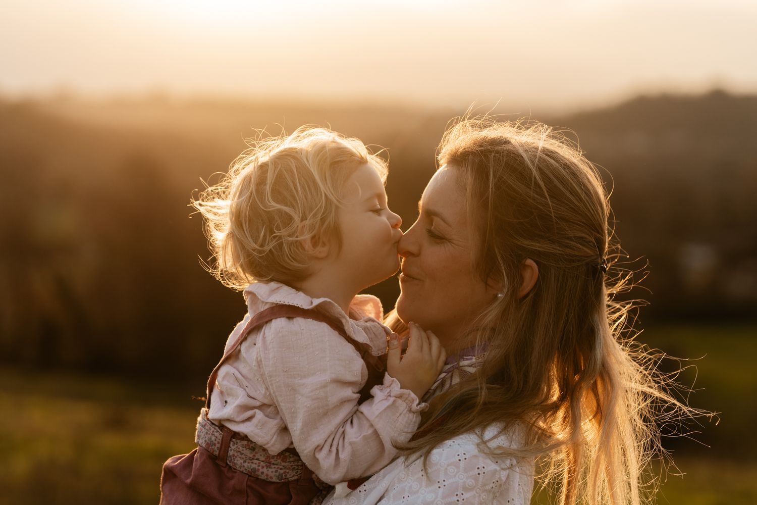Séance photo famille en Isère : une mère et son bébé partagent un tendre bisou d'esquimau dans une prairie au coucher du soleil.
