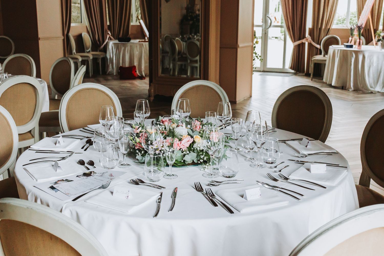 Round wedding reception table elegantly set with white linens, glassware, and a floral centerpiece.