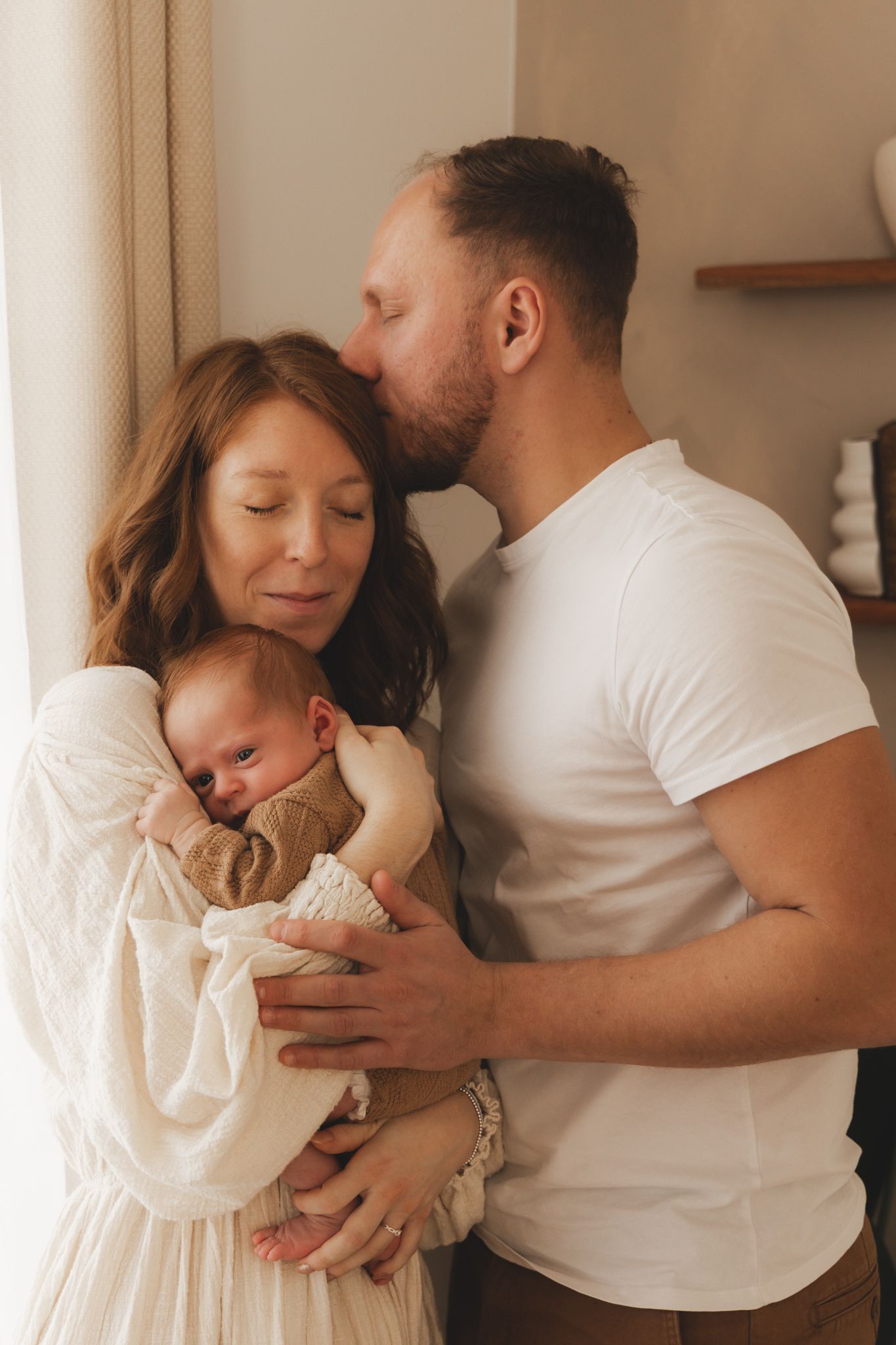 New parents sharing a tender moment, father kissing mother's head while she holds their newborn.