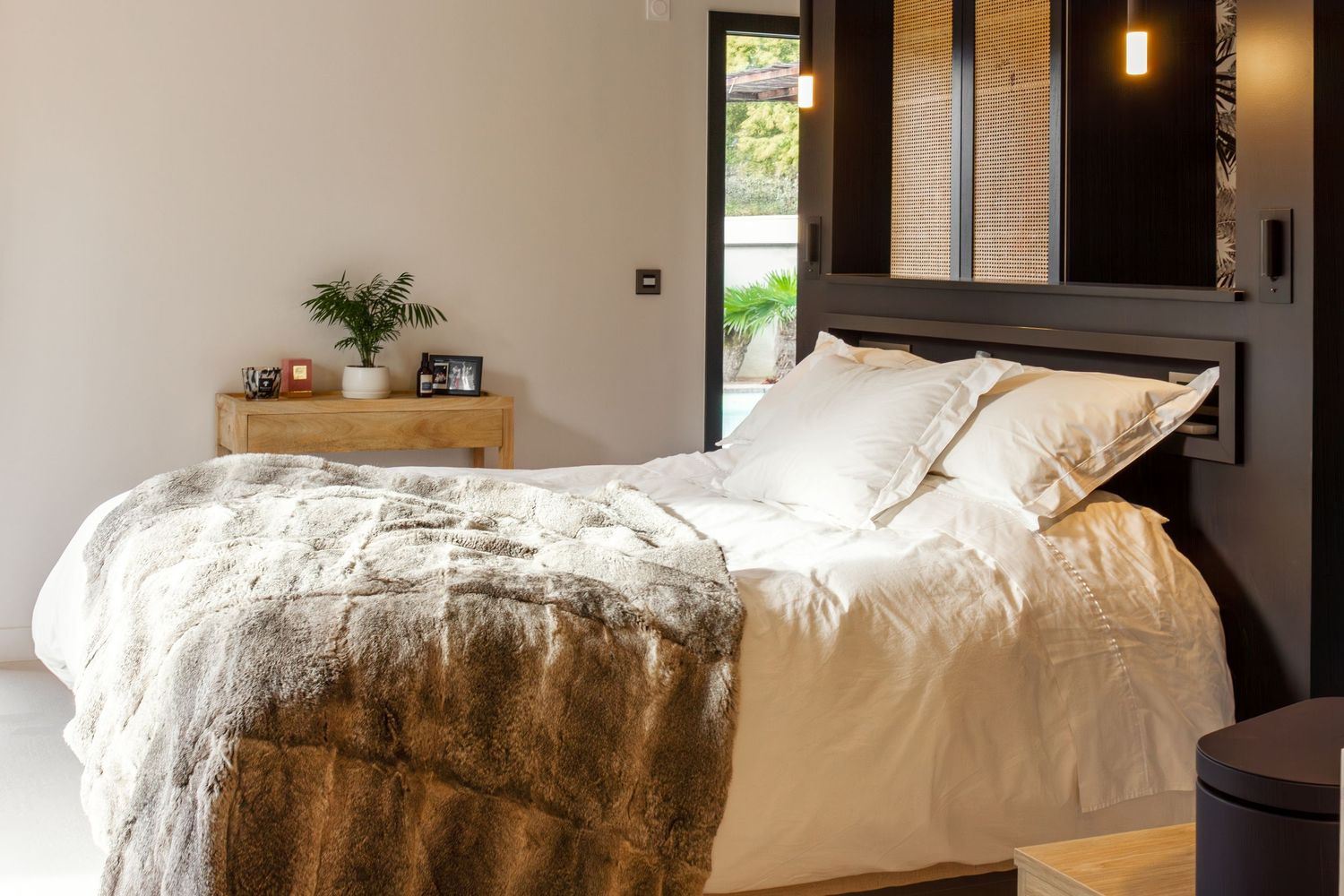Cozy bedroom with white bedding, faux fur throw, wooden nightstand, and pendant light.