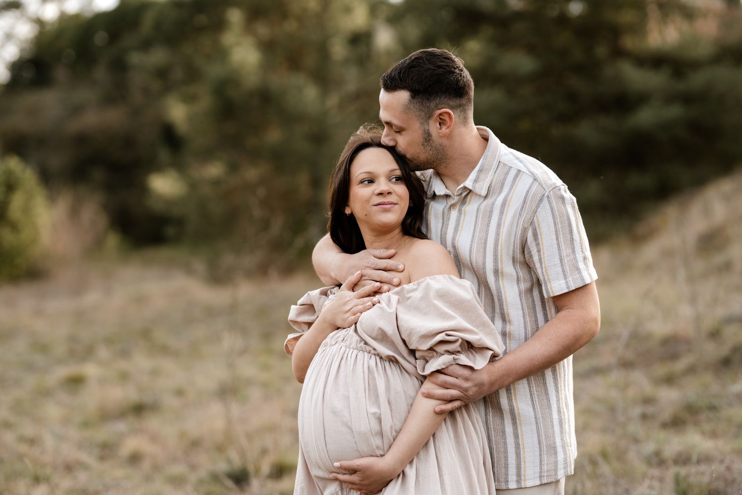 Photo de grossesse en Isère : un instant de pure tendresse avec un futur papa embrassant sa femme en pleine nature.