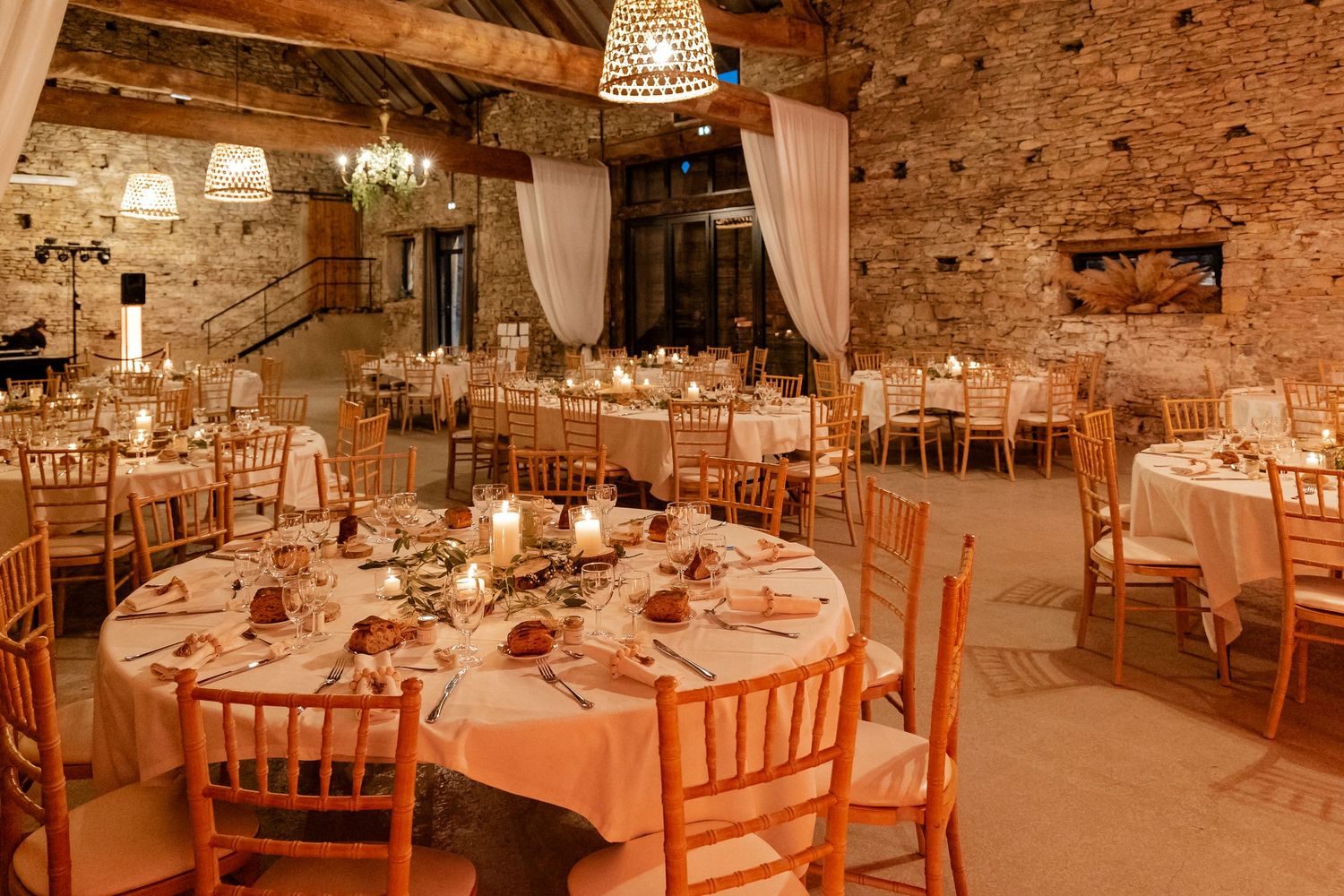 Rustic stone barn wedding reception hall with round tables, gold Chiavari chairs, and candlelight ambiance.