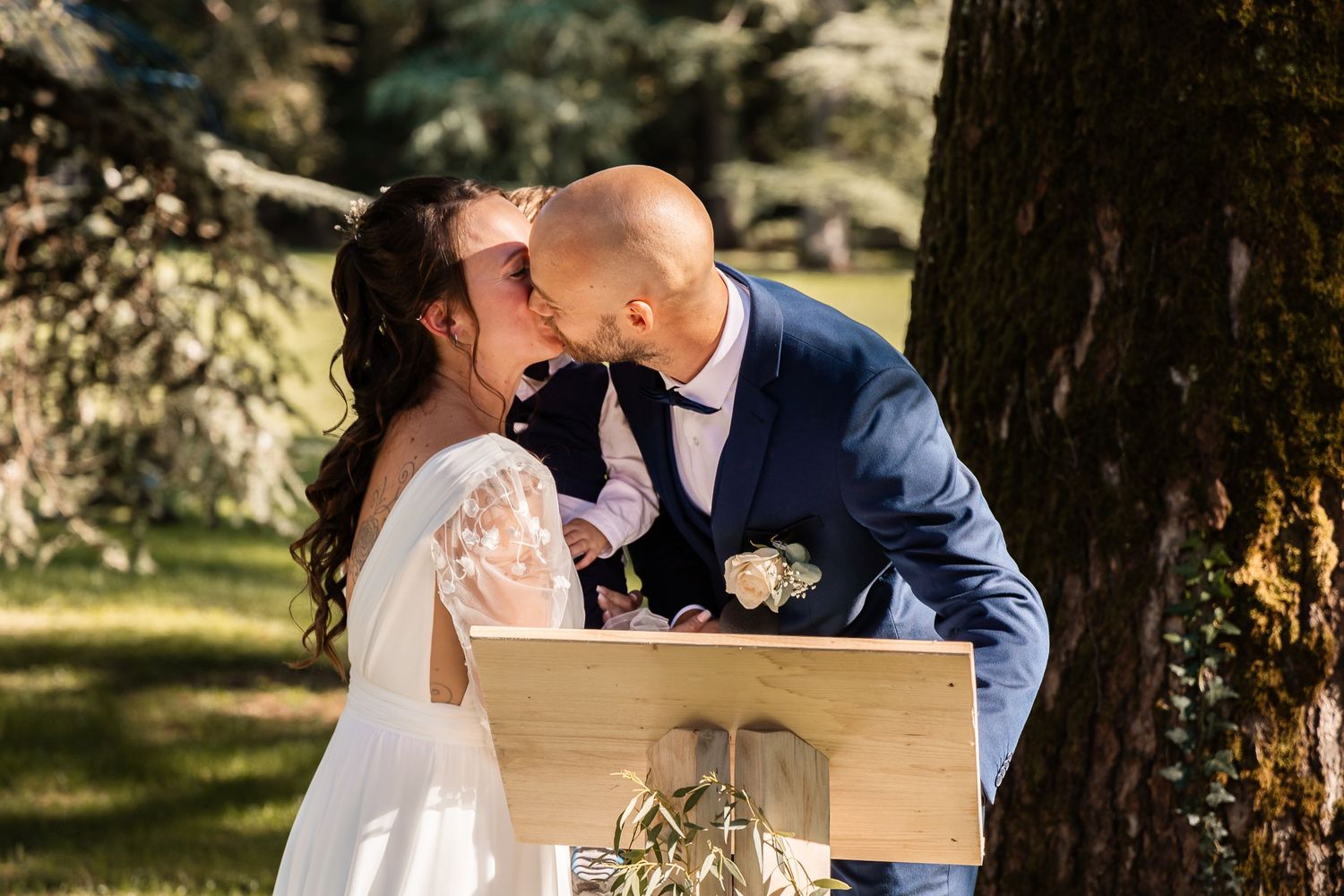 Bride and groom share a romantic kiss beside a wooden podium during their outdoor garden wedding.