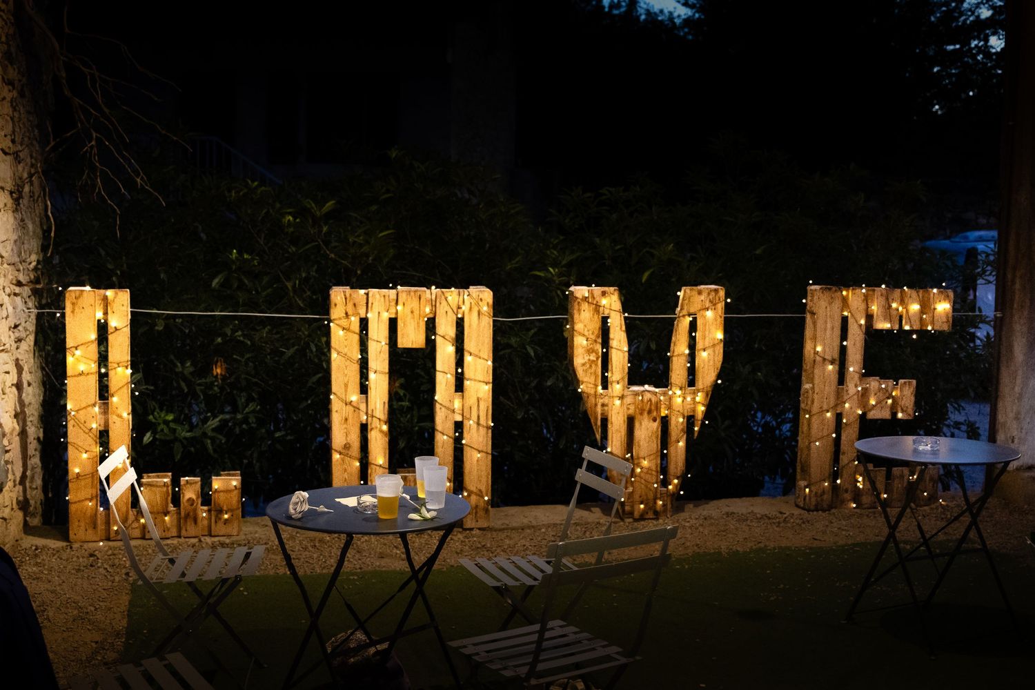 Large illuminated LOVE letters with string lights in outdoor garden wedding night setting with bistro tables.
