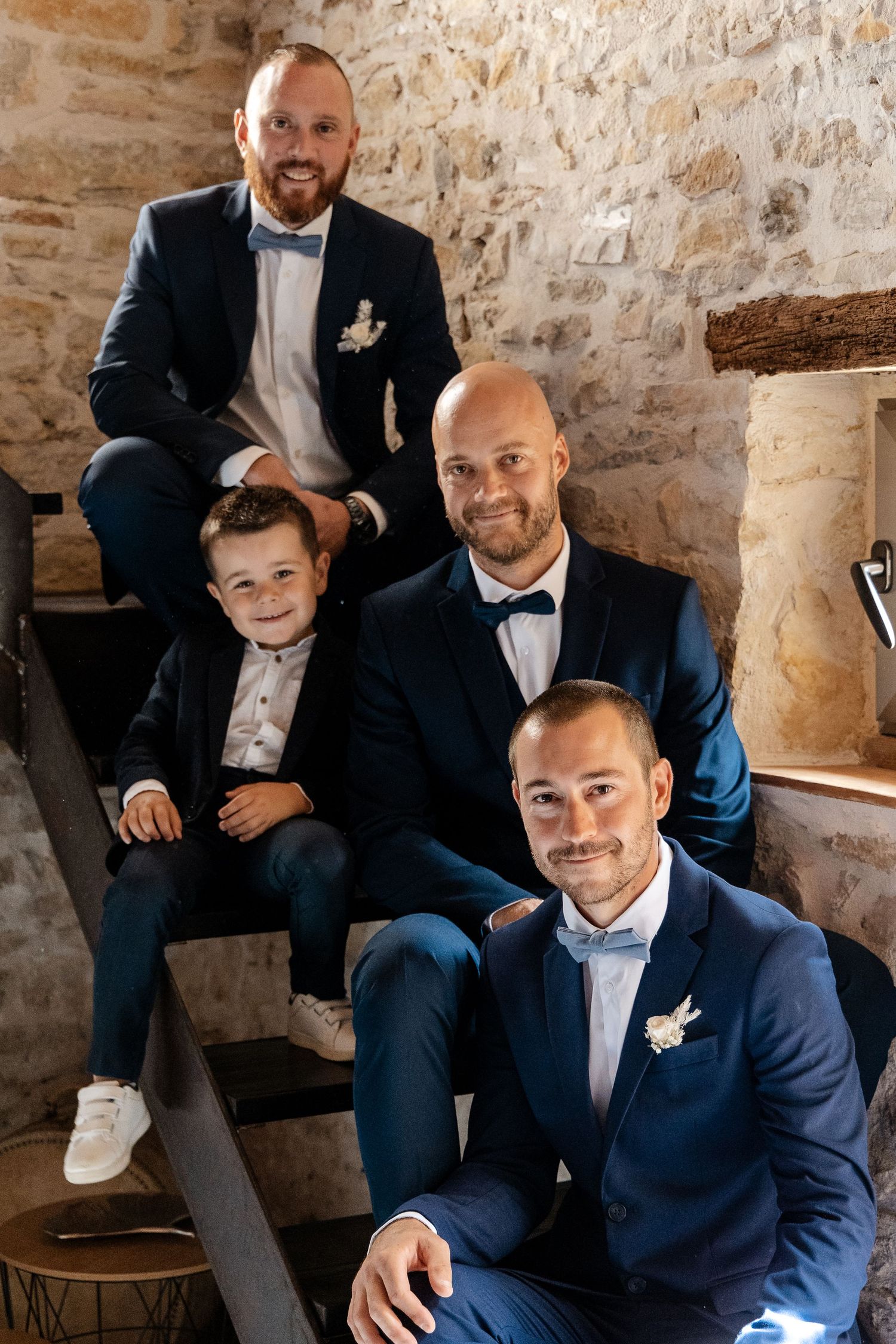 Four males in navy suits posing on stone stairs at a rustic wedding venue.