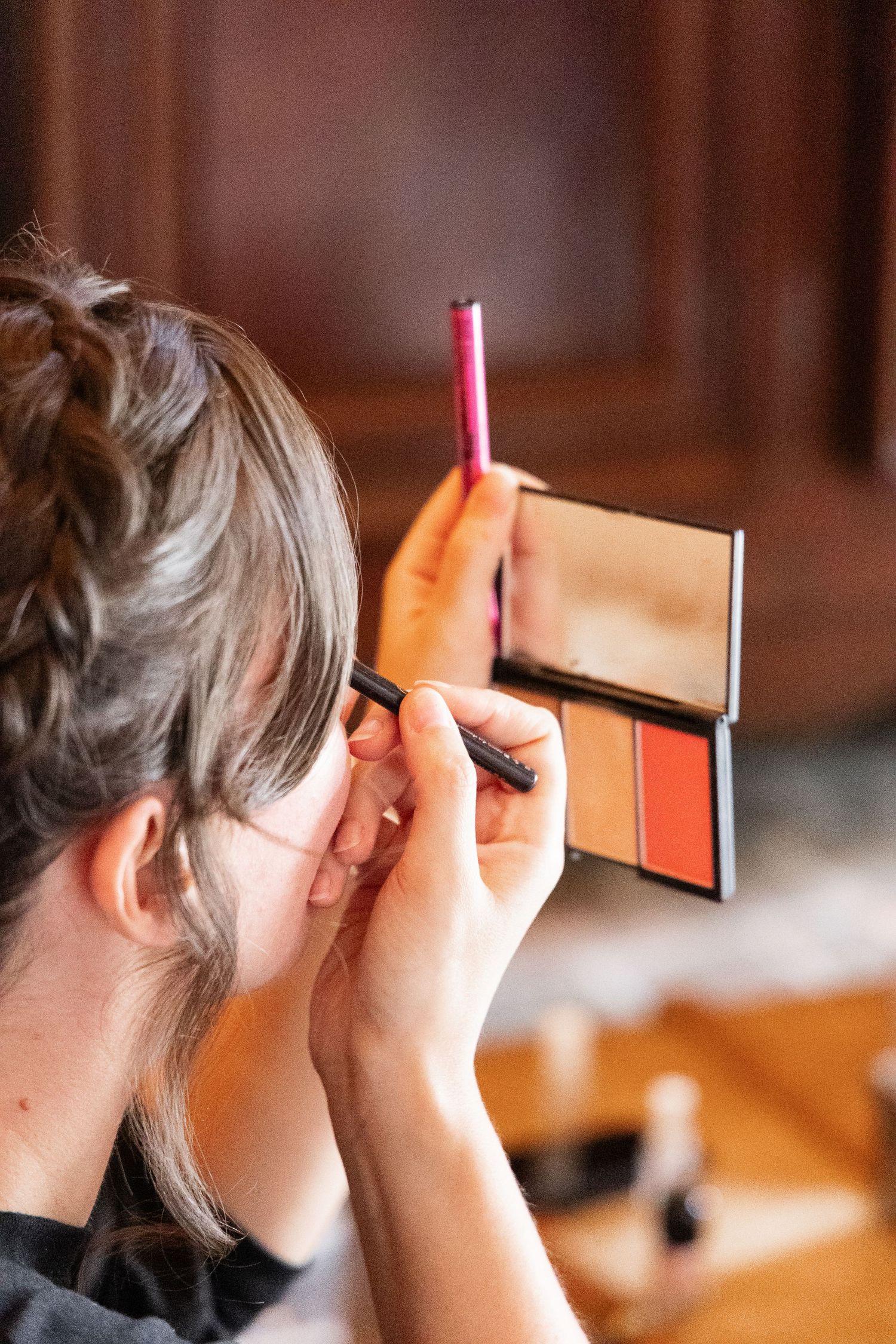 Bridesmaid applying eye makeup using compact mirror and brush during wedding morning preparations.