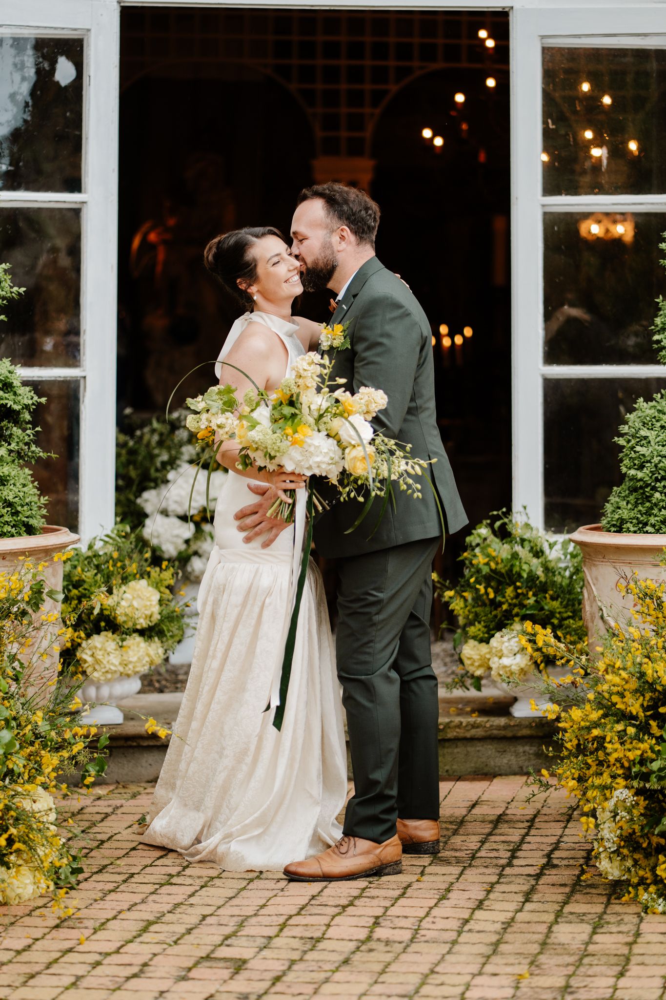 Smiling bride and groom sharing romantic moment outside decorated venue entrance with string lights.