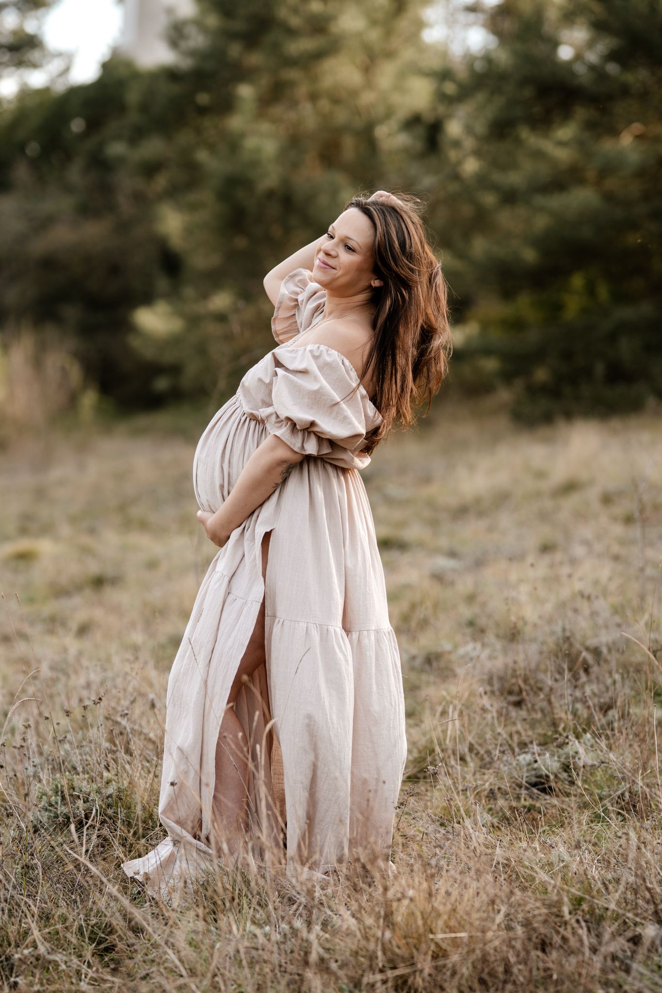 Photo de grossesse en Isère : portrait lumineux d'une future maman en robe beige au milieu d'un champ en pleine nature.