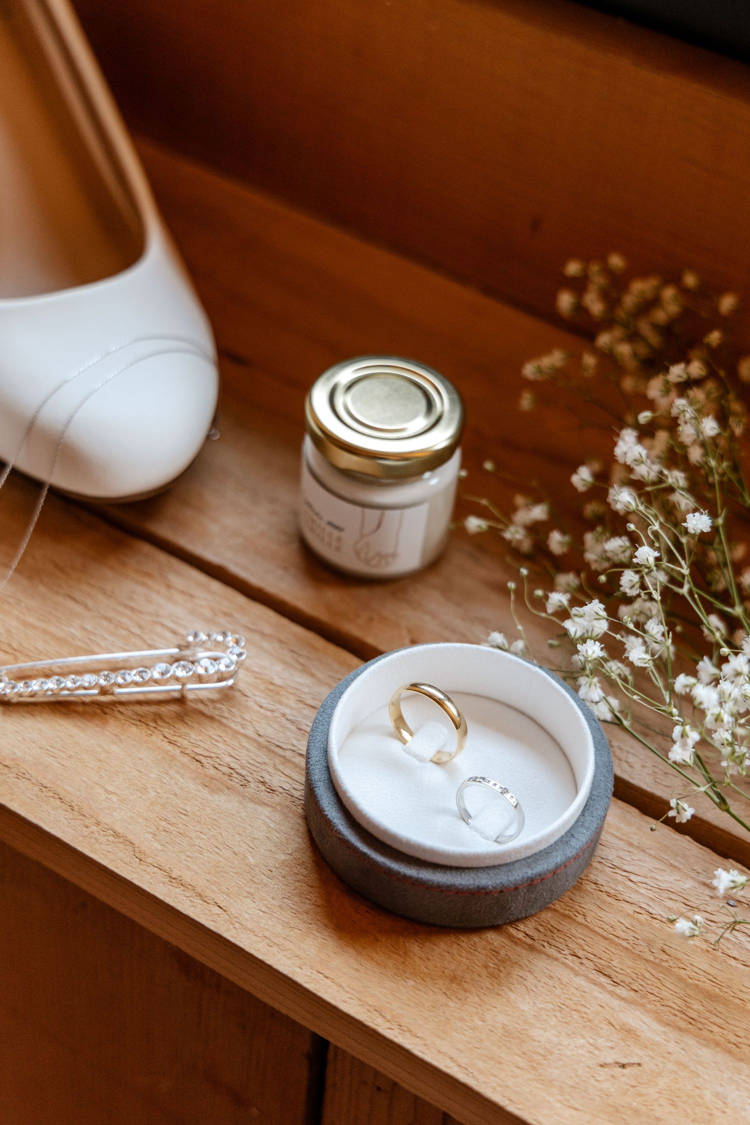 Close-up of two wedding rings in a gray velvet box beside white bridal shoes.
