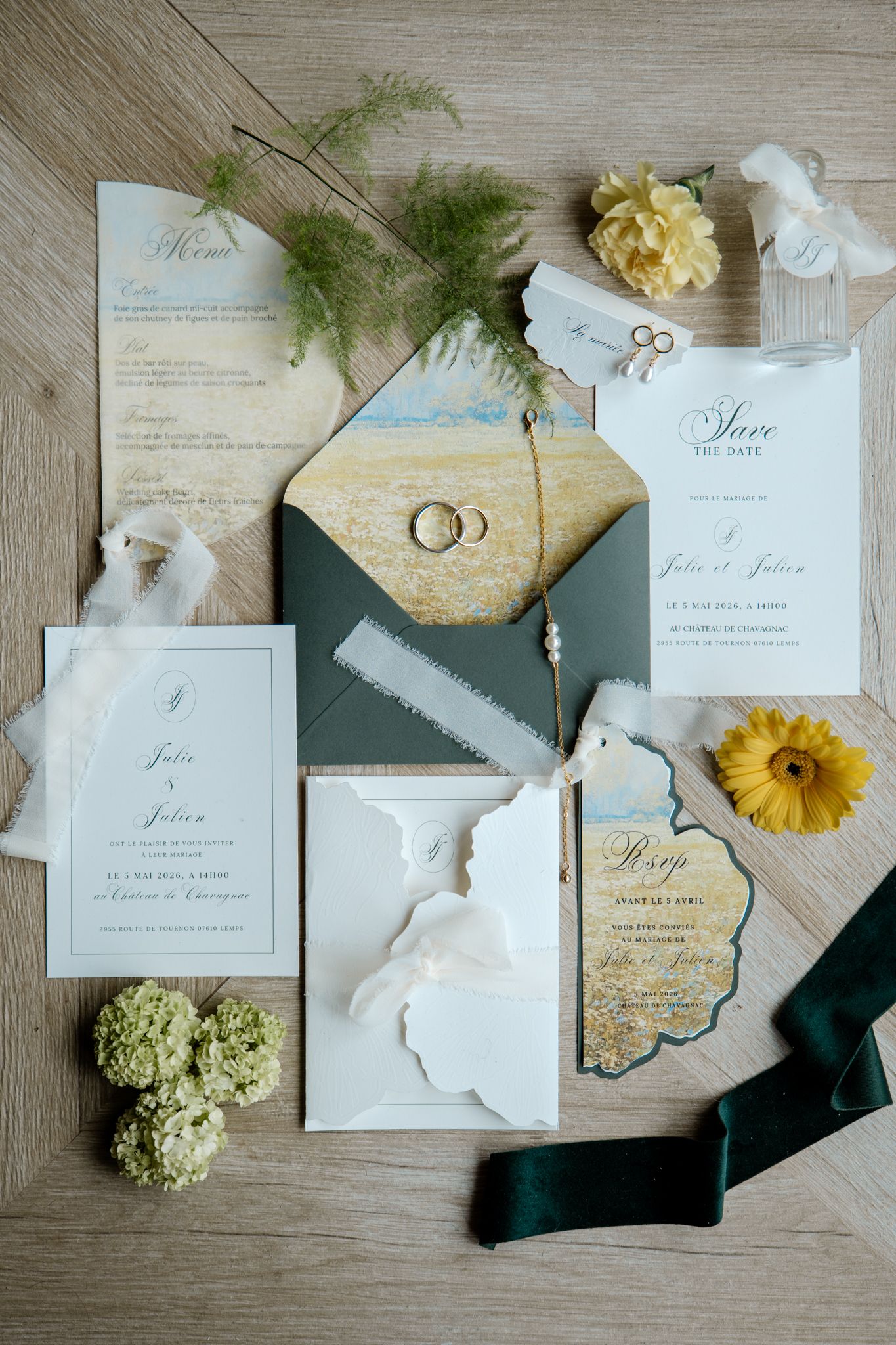 Wedding stationery flatlay with green envelopes, rings, yellow flowers, and invitation suite.