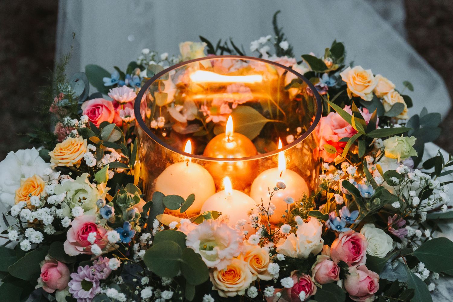 Elegant wedding unity candle arrangement with glowing candles surrounded by colorful roses and greenery.