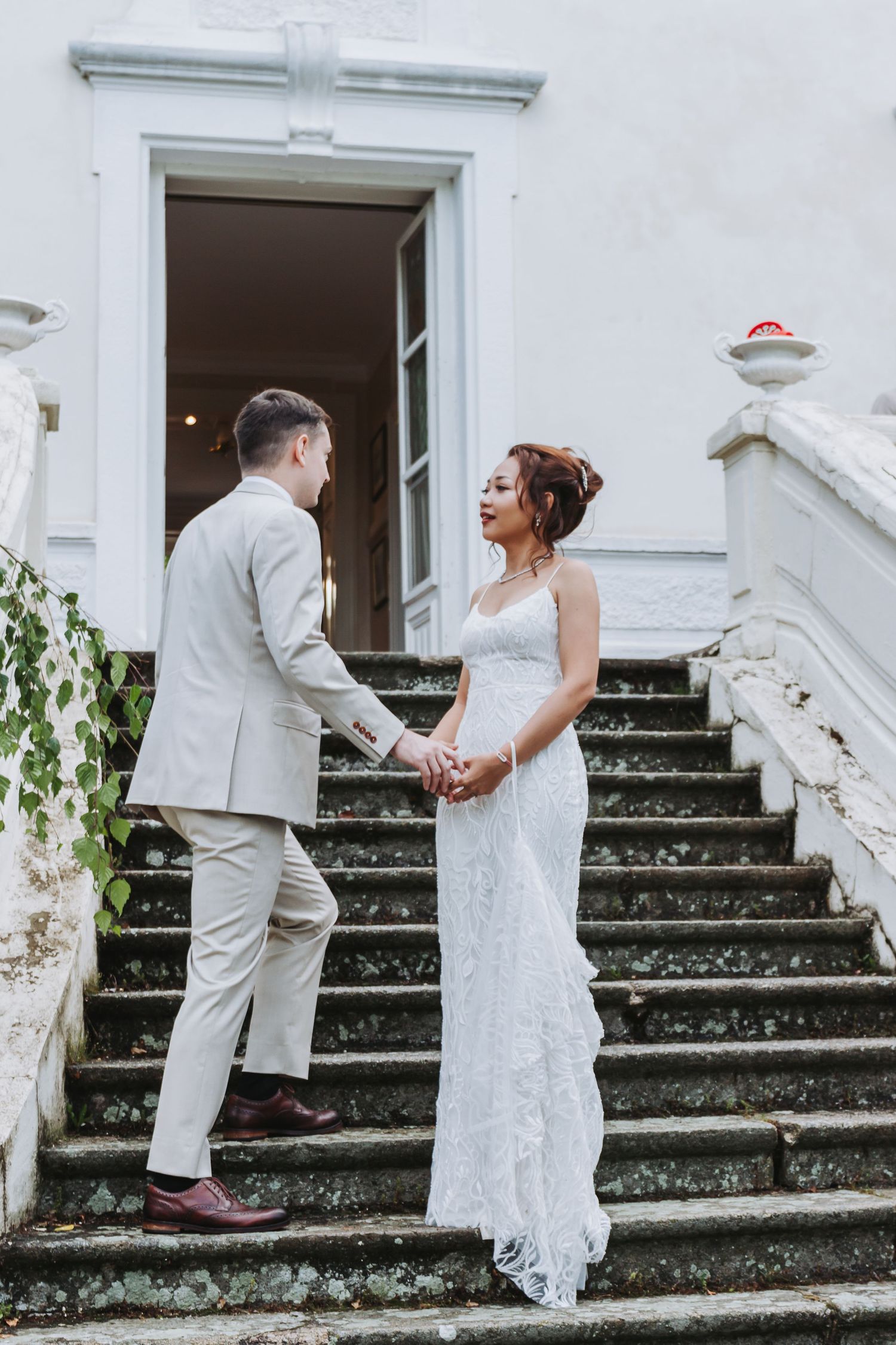 Bride and groom holding hands on stone staircase outside elegant white building during wedding portraits.