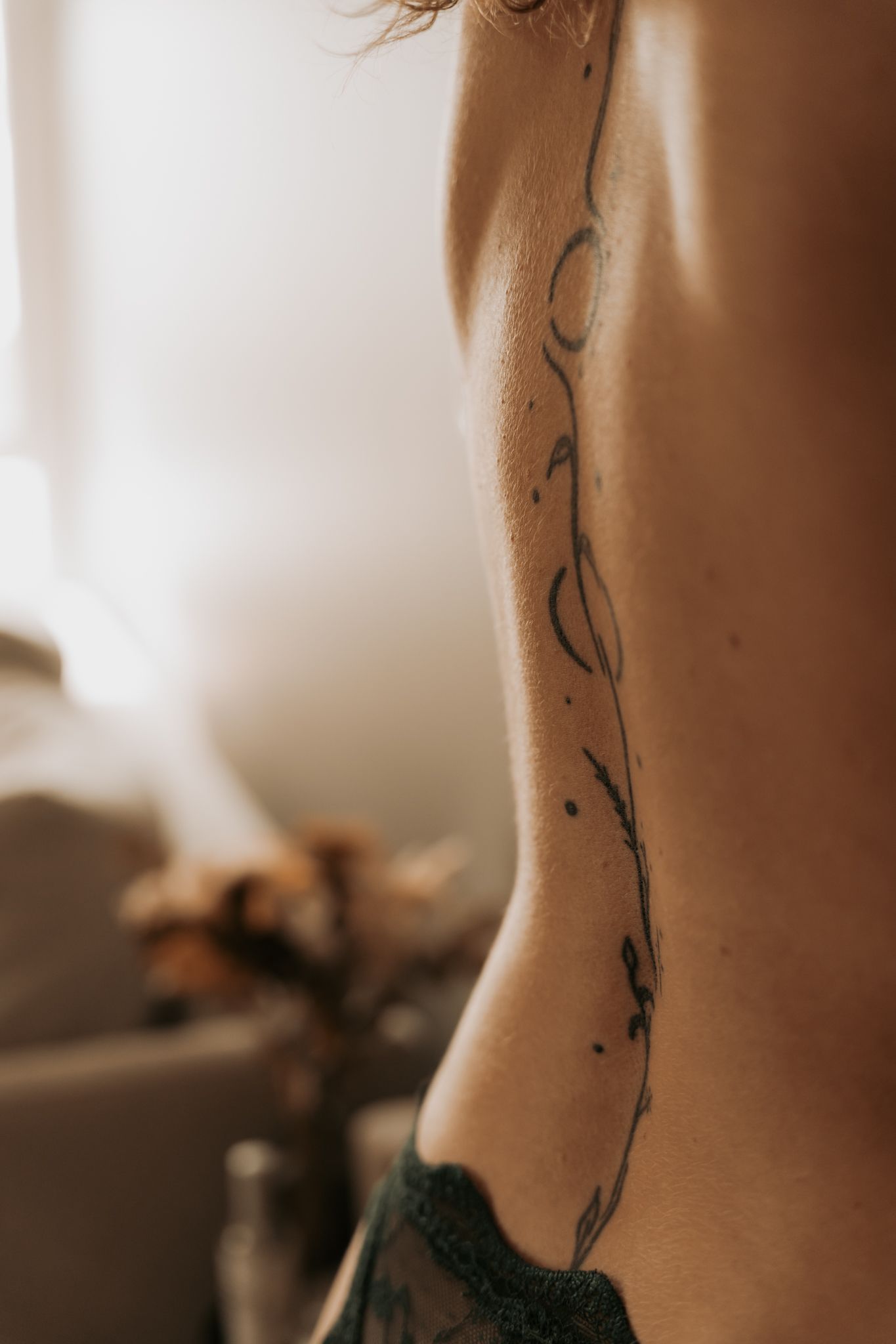 Séance photo boudoir en Isère : l'élégance d'un profil et la finesse d'un tatouage végétal sur le dos.