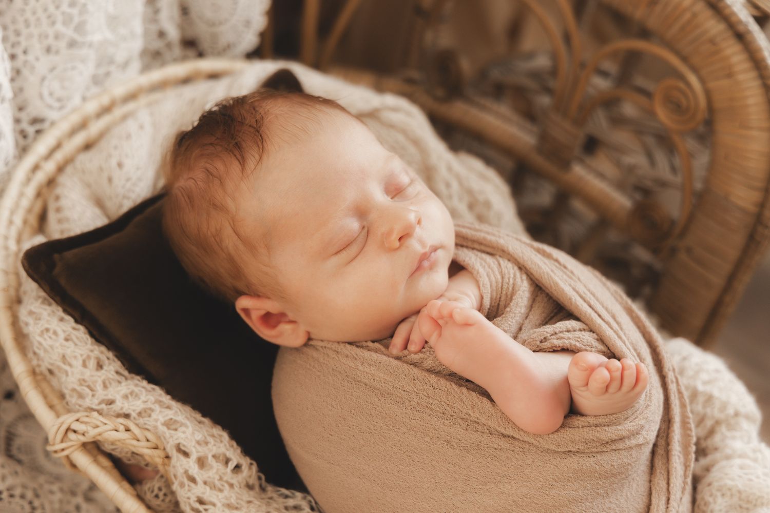 Peaceful newborn baby sleeping in wicker bassinet, wrapped in warm beige swaddle.