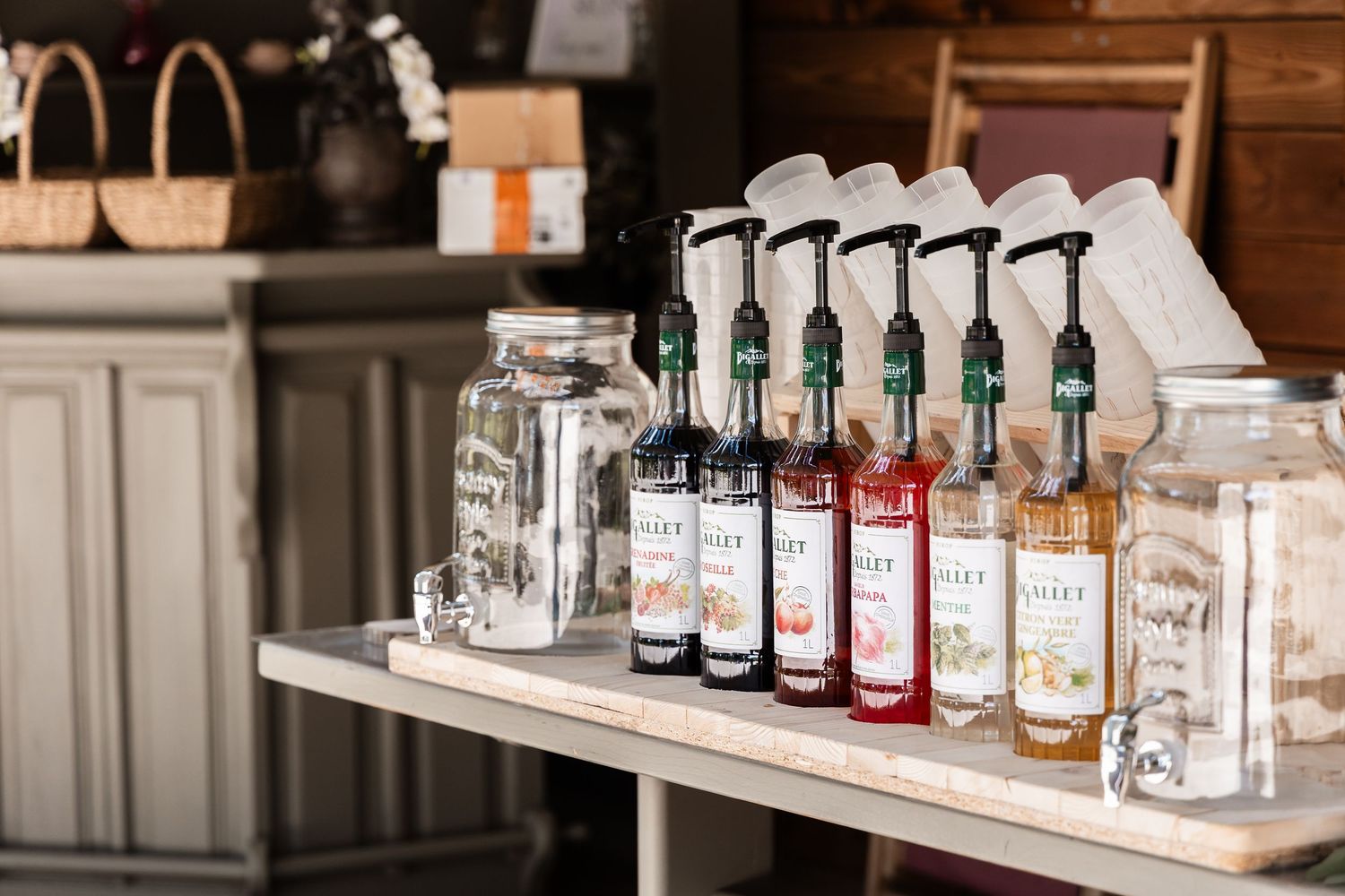 Close-up of colorful Monin syrup bottles with pump dispensers arranged on a white table at a wedding bar.