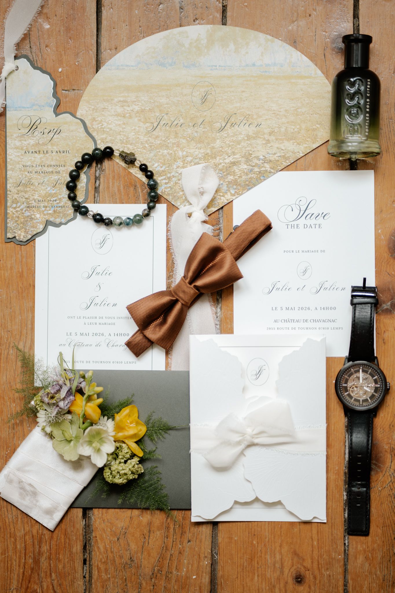 Elegant wedding stationery flat lay with save the date cards, bow tie, watches, and florals.