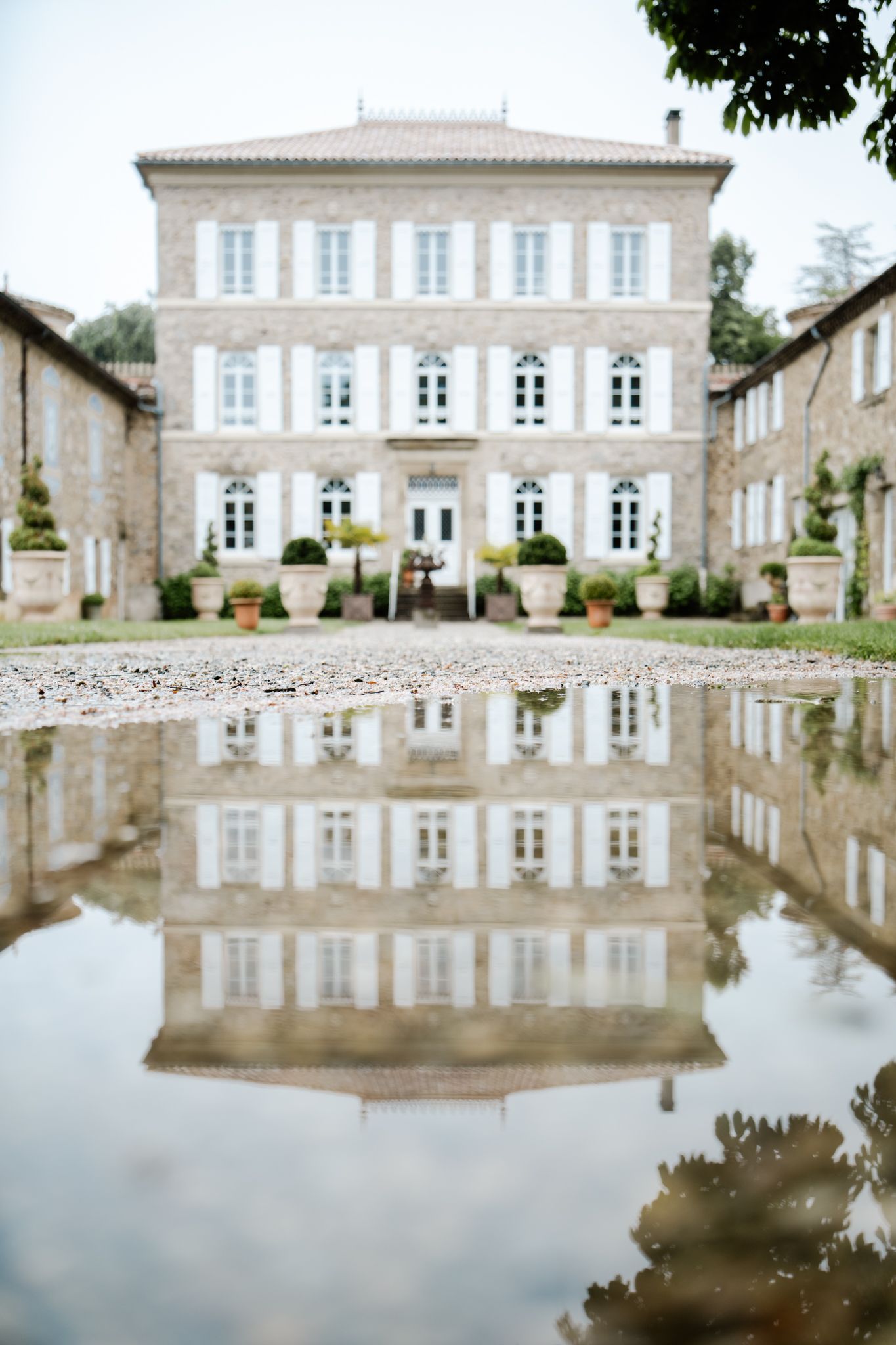 Elegant French chateau reflected in rain puddle on gravel courtyard on overcast day.