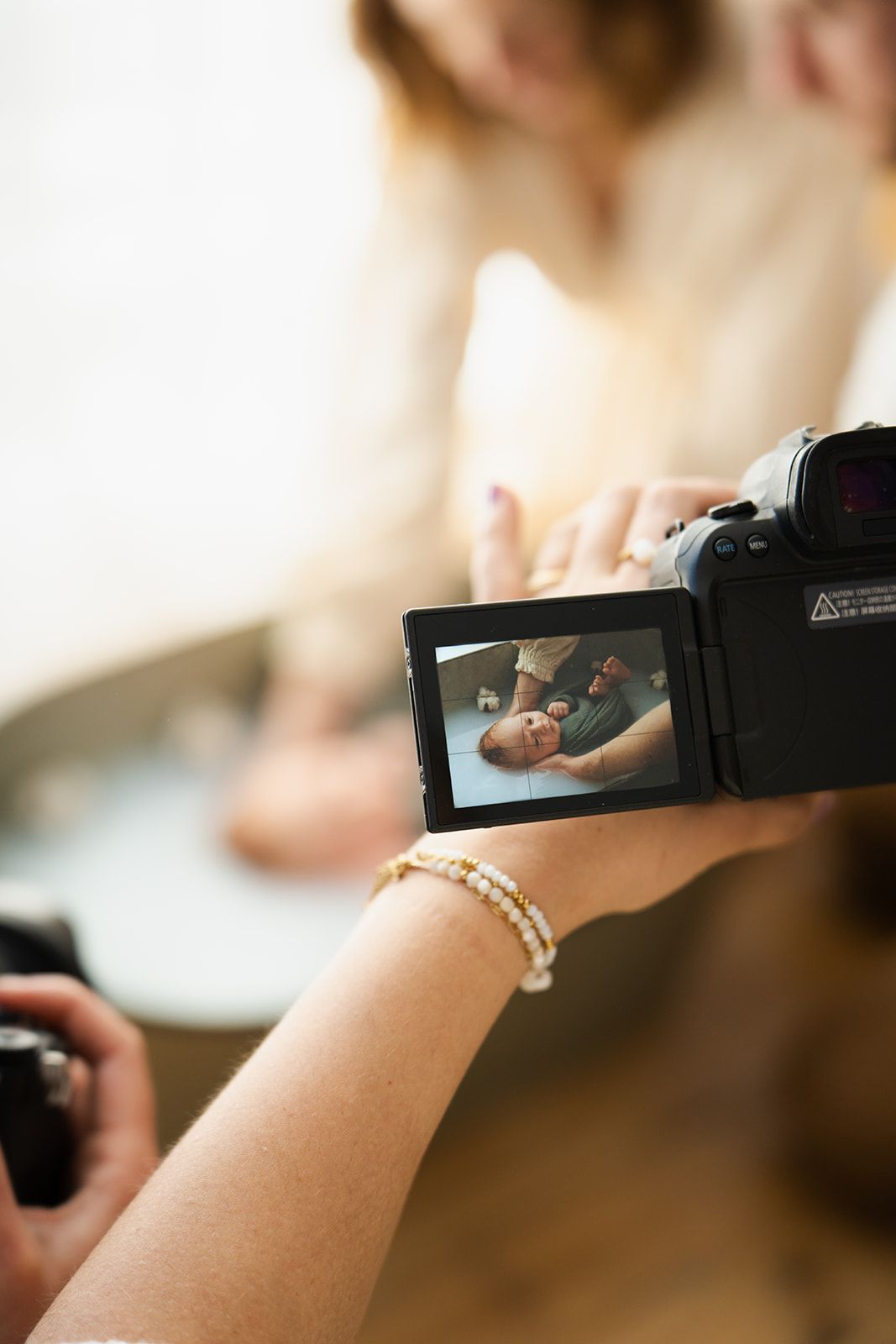 Person filming a newborn baby on a video camera screen during a professional photoshoot session.