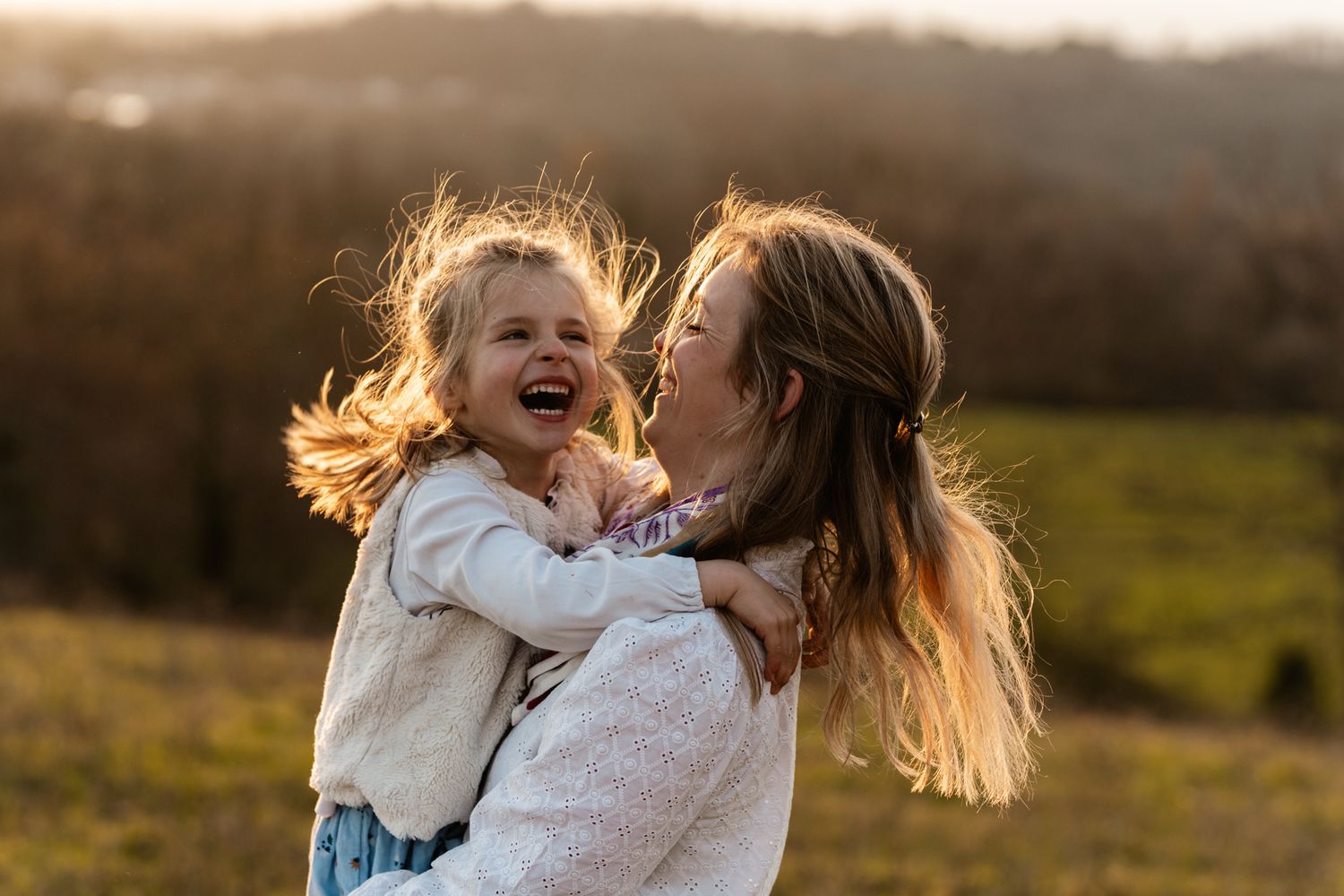 Séance photo famille en Isère : une mère et sa fille partagent un moment de complicité et de rire au coucher du soleil.