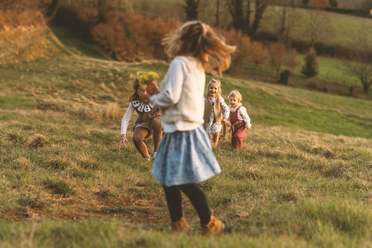 Children running and playing joyfully on a green hillside in warm autumn sunlight.