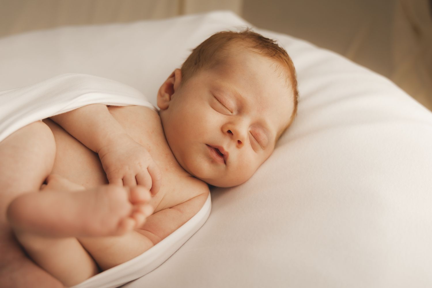 Serene newborn baby sleeping on white pillow, arms folded on chest.