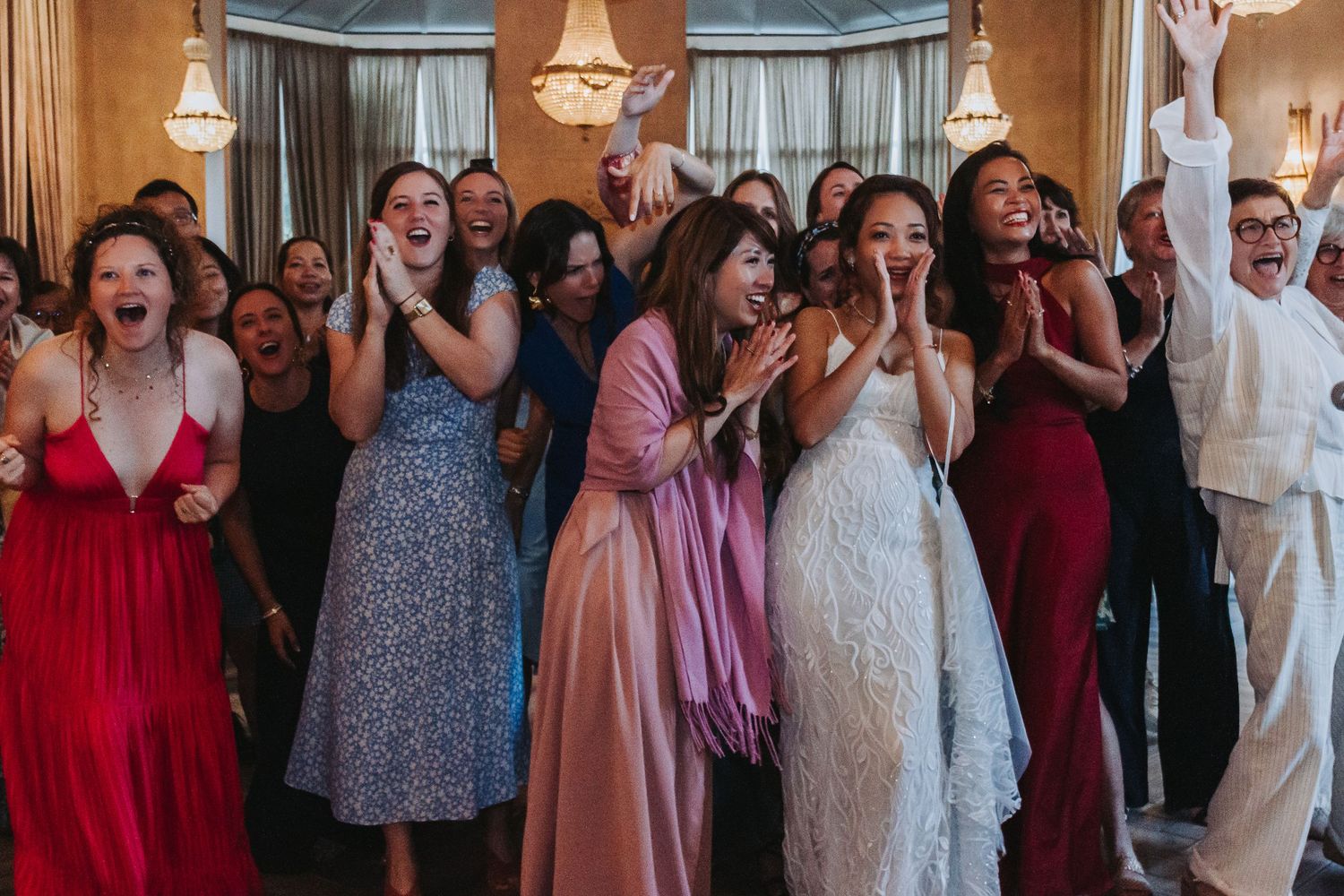 Joyful bride and wedding guests cheering and celebrating together in decorated reception hall.