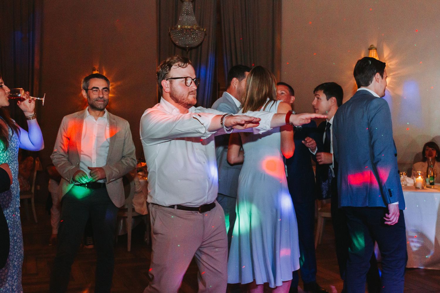 Wedding guests dancing and socializing under colorful disco lights at festive reception.