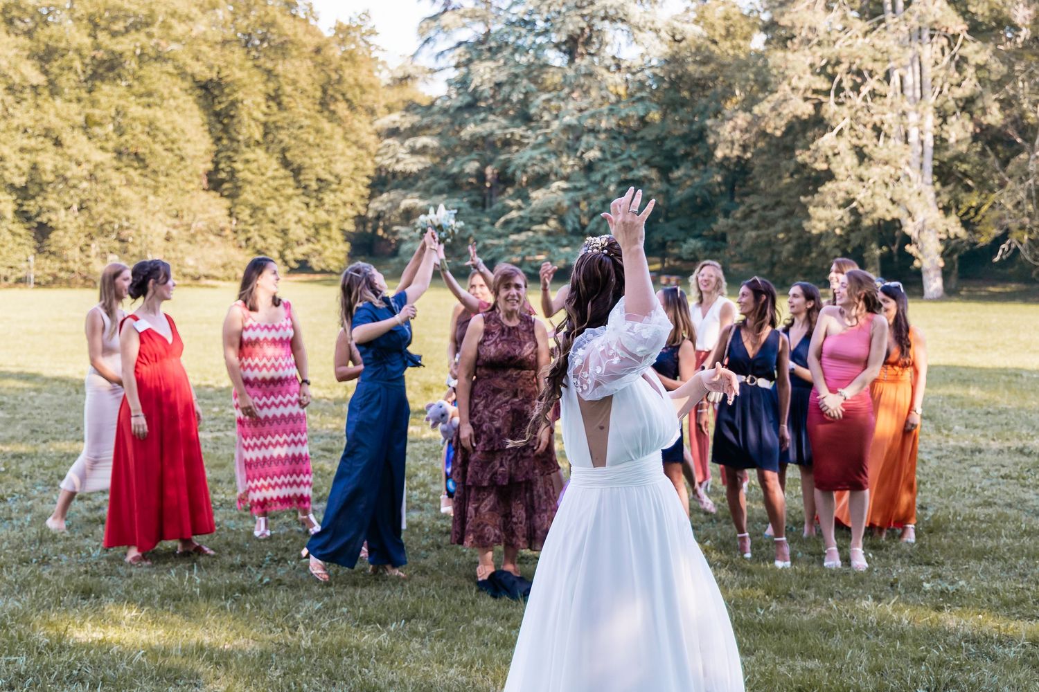 Bride tosses her bouquet to a group of excited female guests during an outdoor wedding reception.