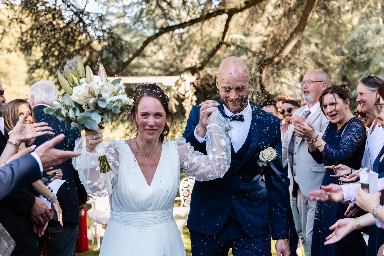 Newlyweds walk joyfully through a shower of confetti thrown by cheering guests after outdoor ceremony.