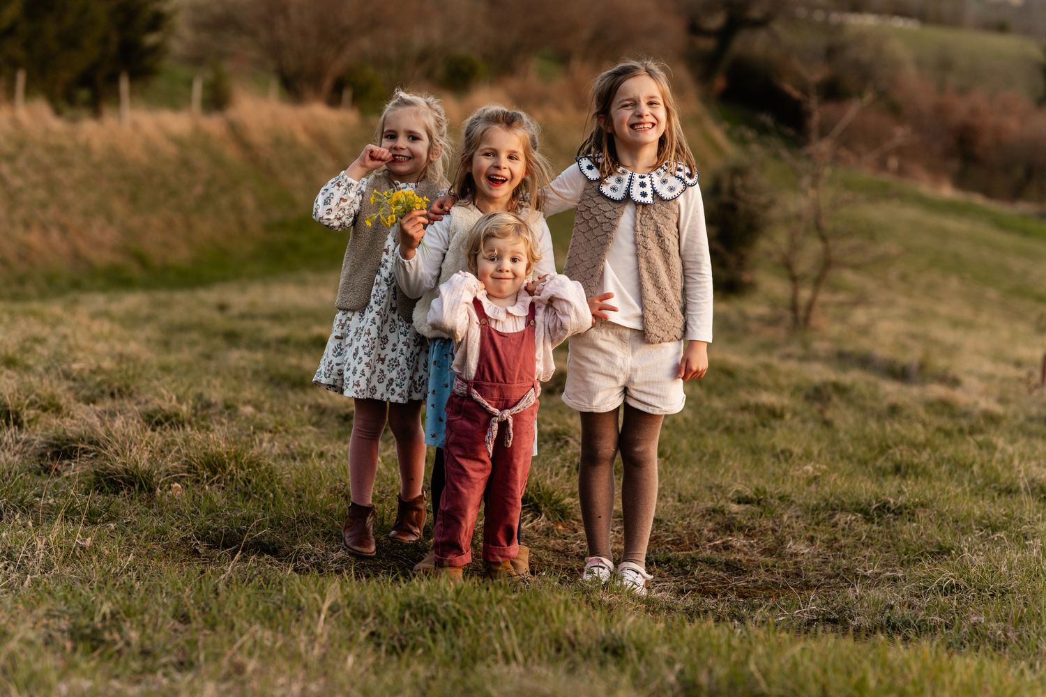 Séance photo famille en Isère : quatre jeunes filles s'amusant dans une prairie au coucher du soleil.