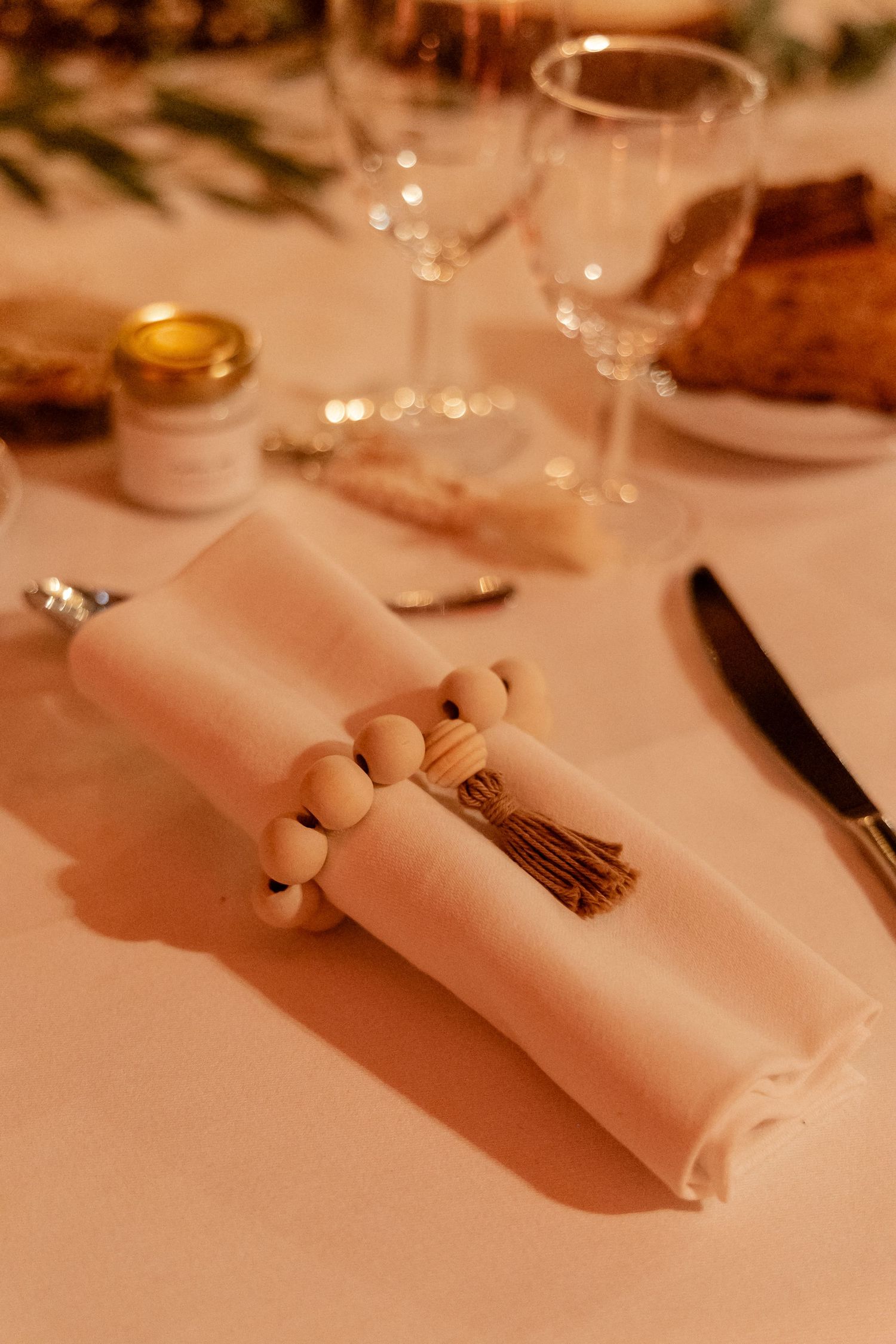 Elegant wedding table setting with beaded napkin ring, tassel, wine glass, and knife on white linen.