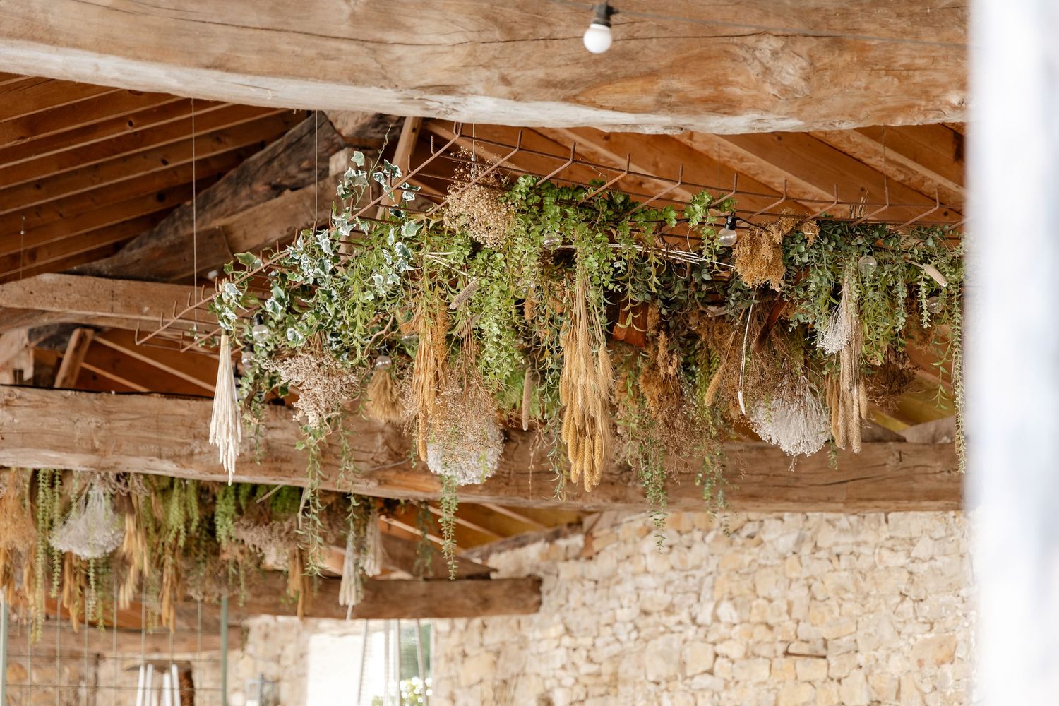 Dried herbs and greenery hanging from rustic wooden ceiling beams in a stone-walled French countryside venue.