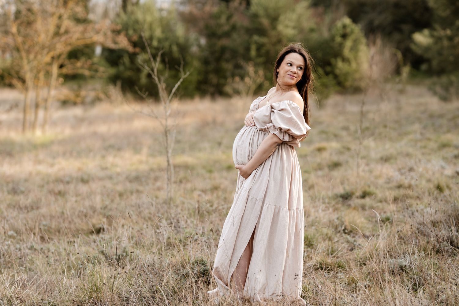Photo de grossesse en Isère : l'élégance d'une future maman en robe beige et épaules dénudées au cœur d'un champ naturel.