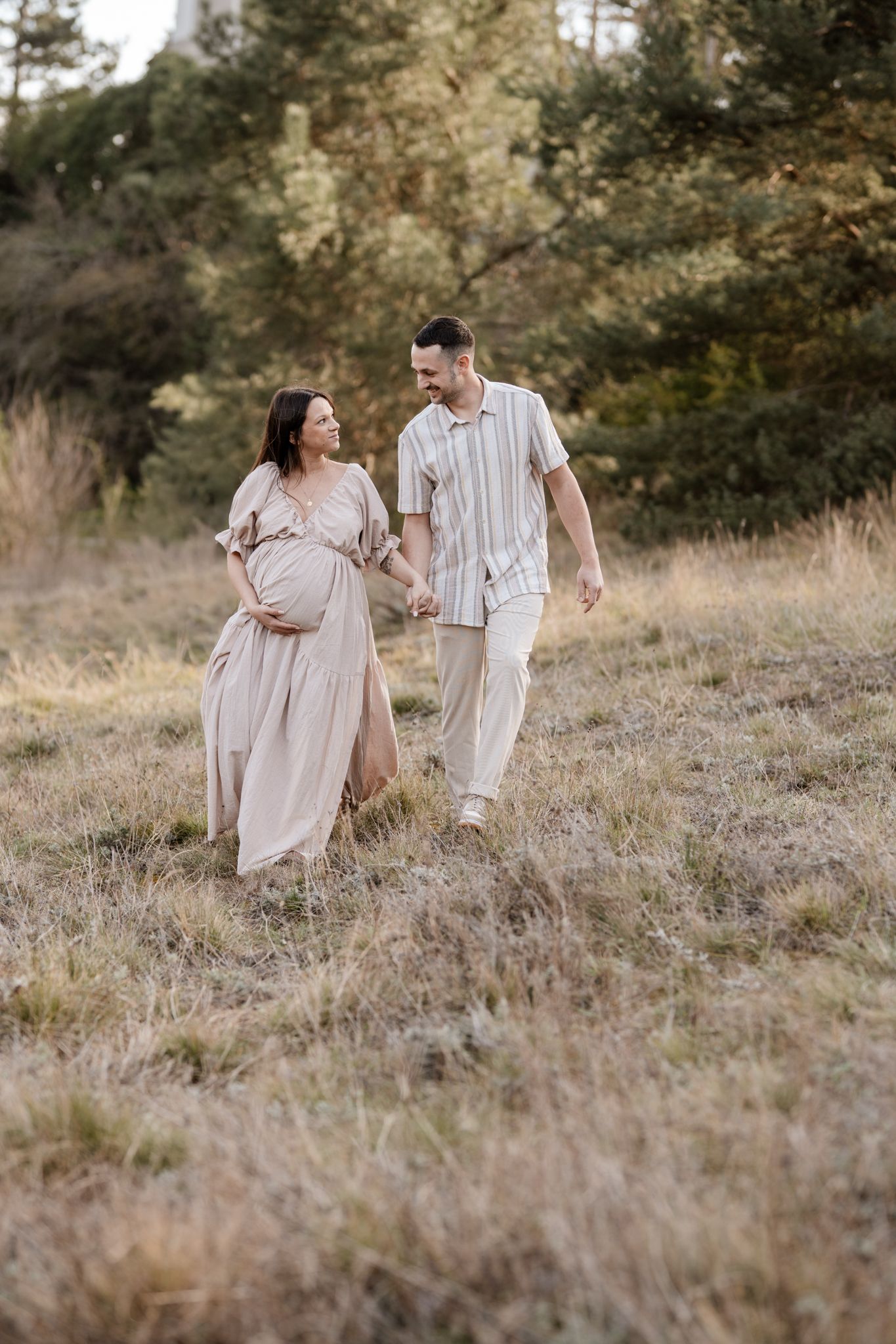 Séance photo couple en Isère : une balade complice main dans la main au cœur d'un champ doré pour fêter l'arrivée de bébé.
