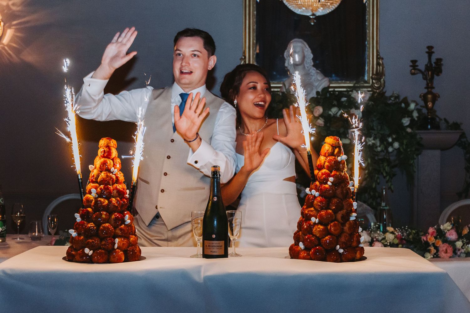 Bride and groom celebrating at wedding table with sparkling croquembouche cake towers and champagne.