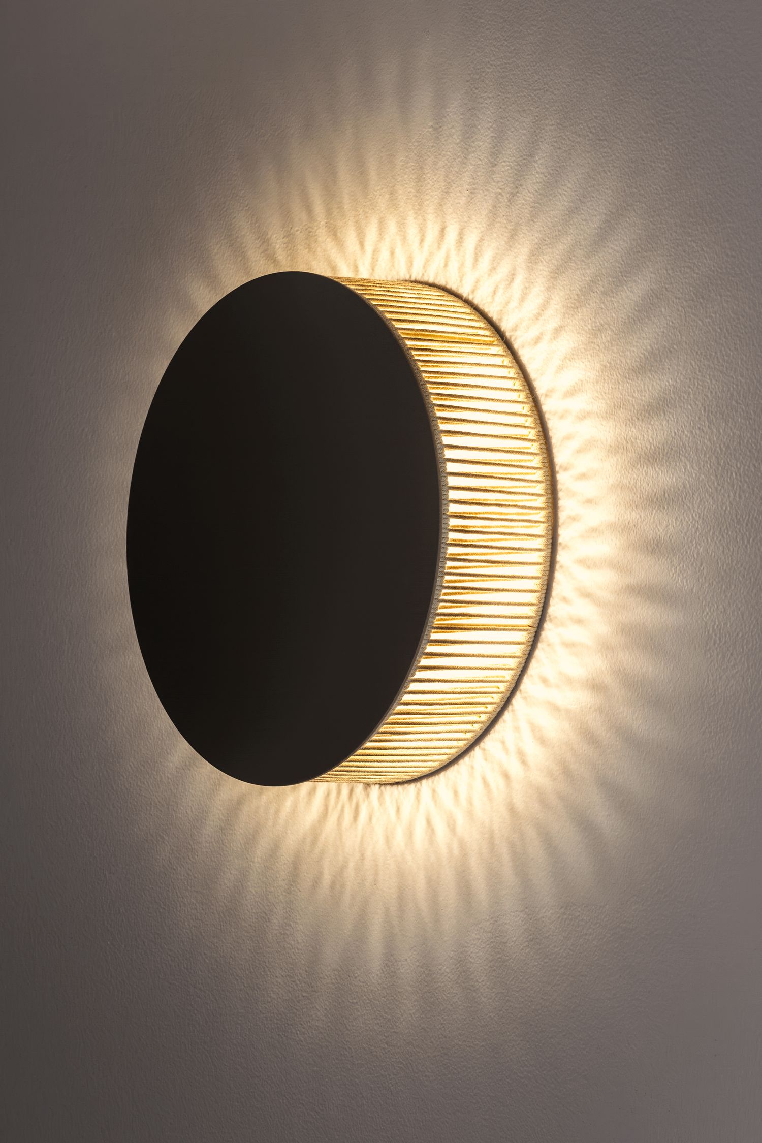 Artistic black and gold crescent moon wall sconce casting warm rays of light on a gray wall.