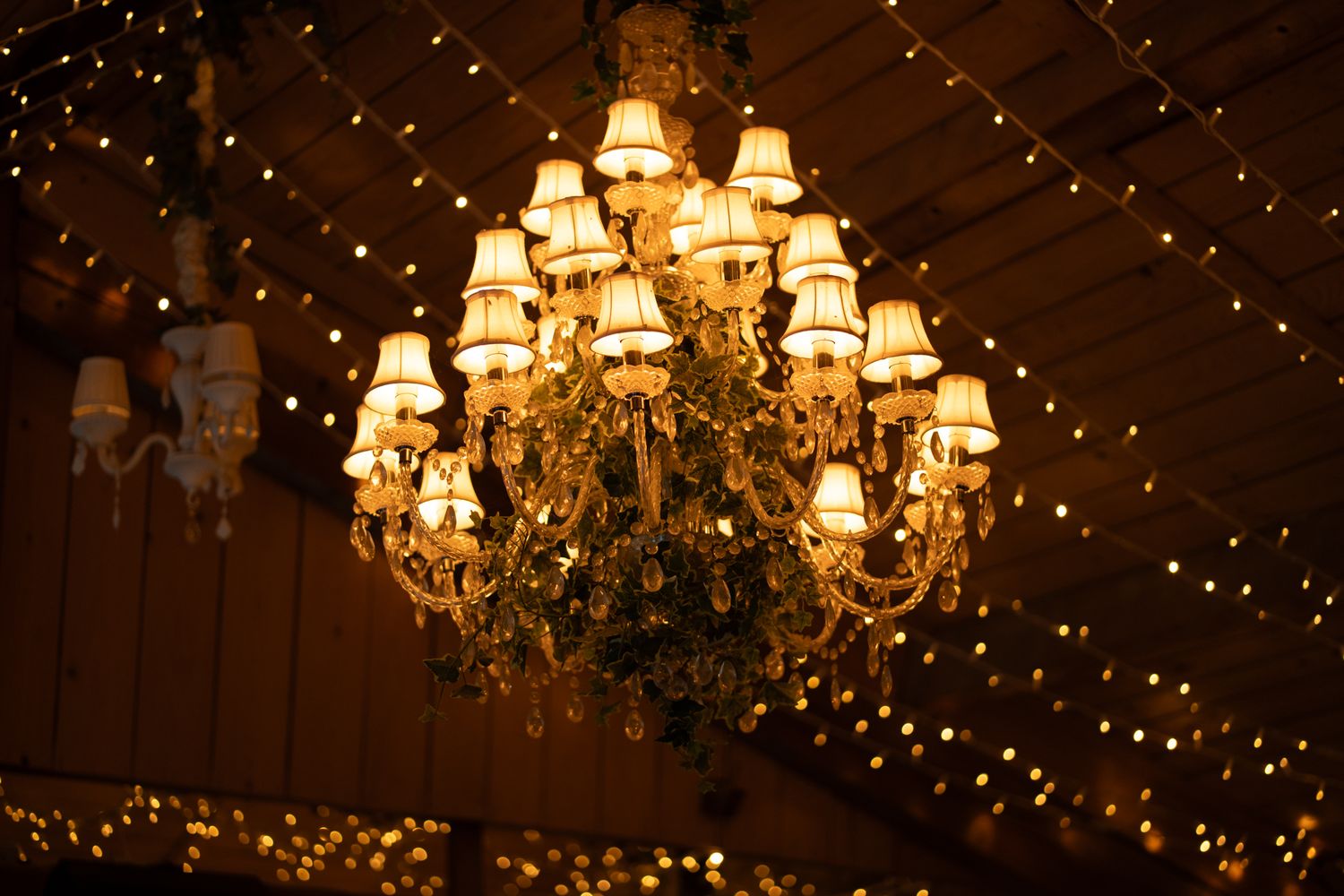 Ornate crystal chandelier with warm glowing lampshades surrounded by fairy lights at wedding venue.