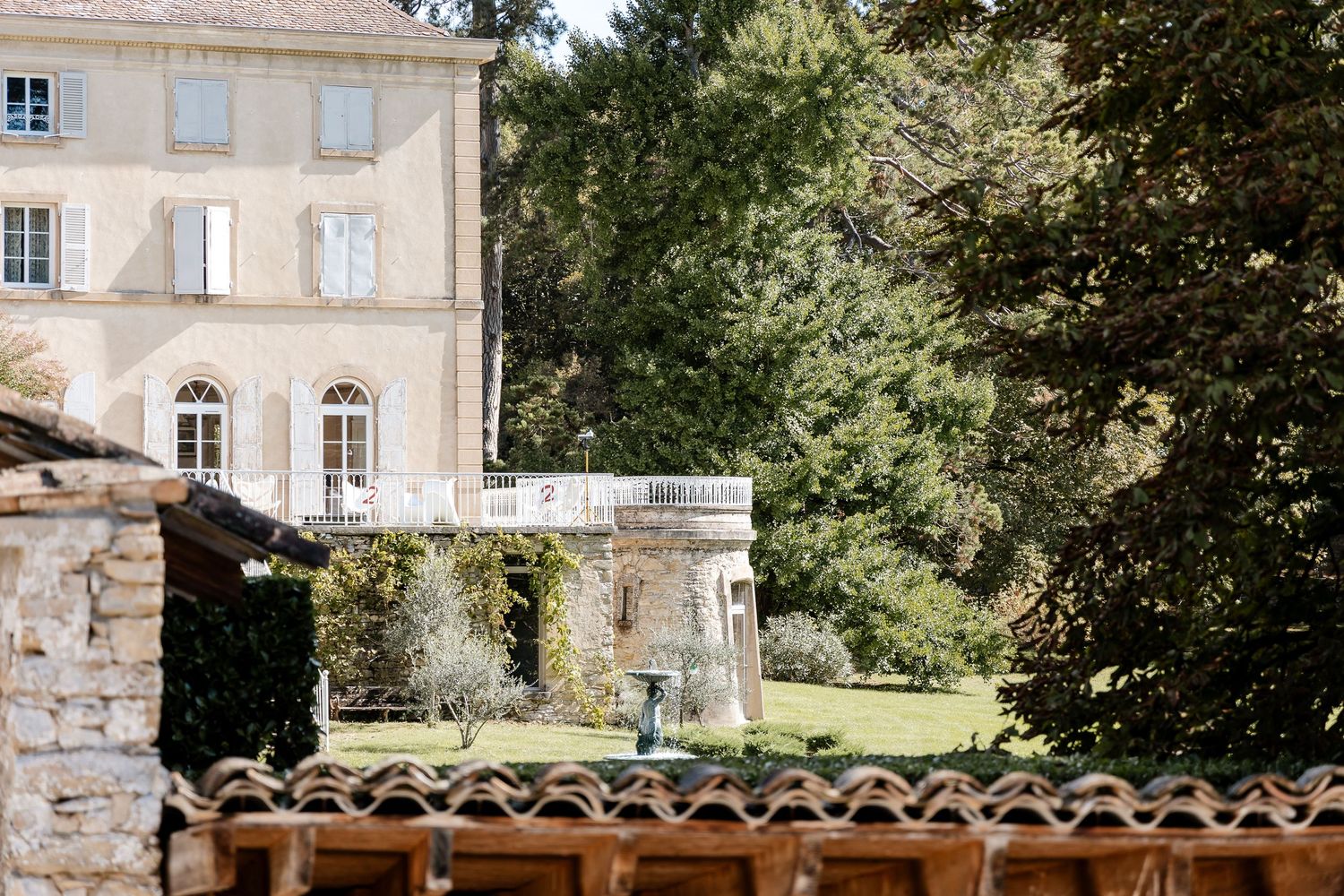 Elegant French chateau with manicured gardens and mature trees viewed from a rustic stone building rooftop.