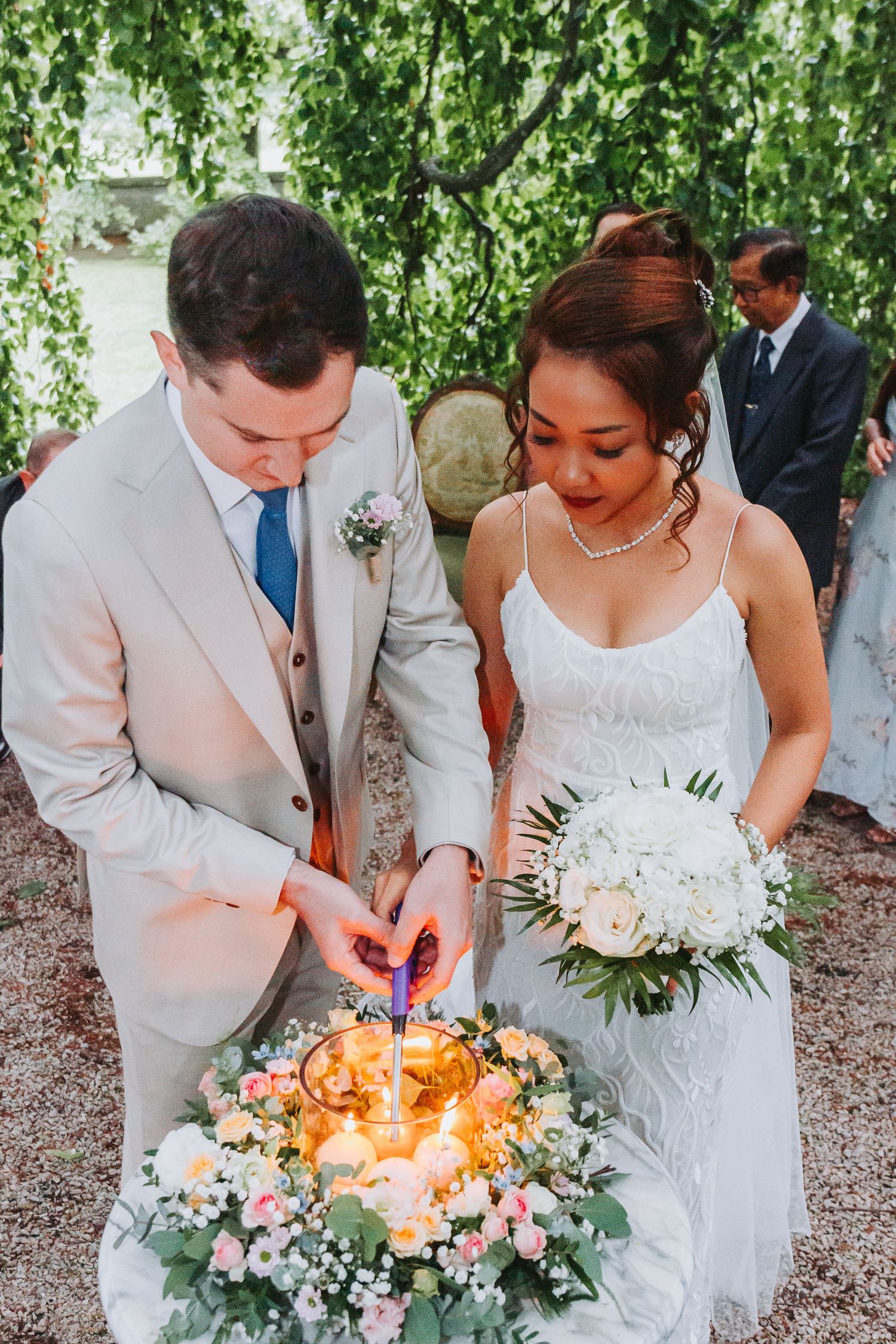 Bride and groom light unity candles surrounded by a floral wreath of roses and greenery during outdoor wedding ceremony.