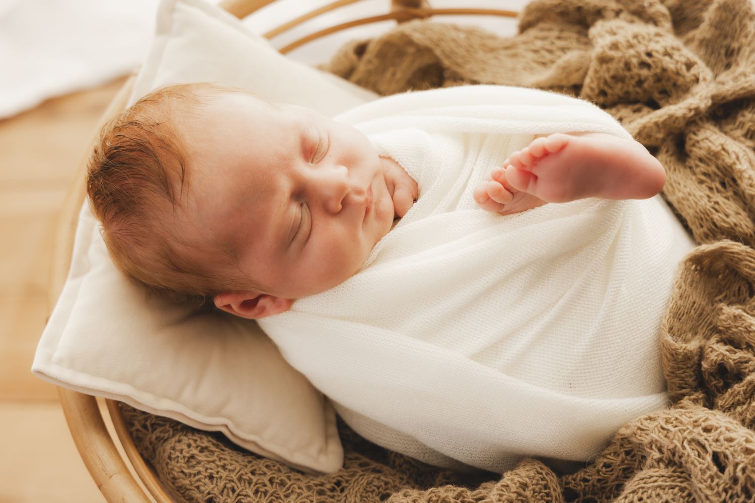 Peaceful newborn baby sleeping swaddled in white wrap inside a cozy wicker basket.
