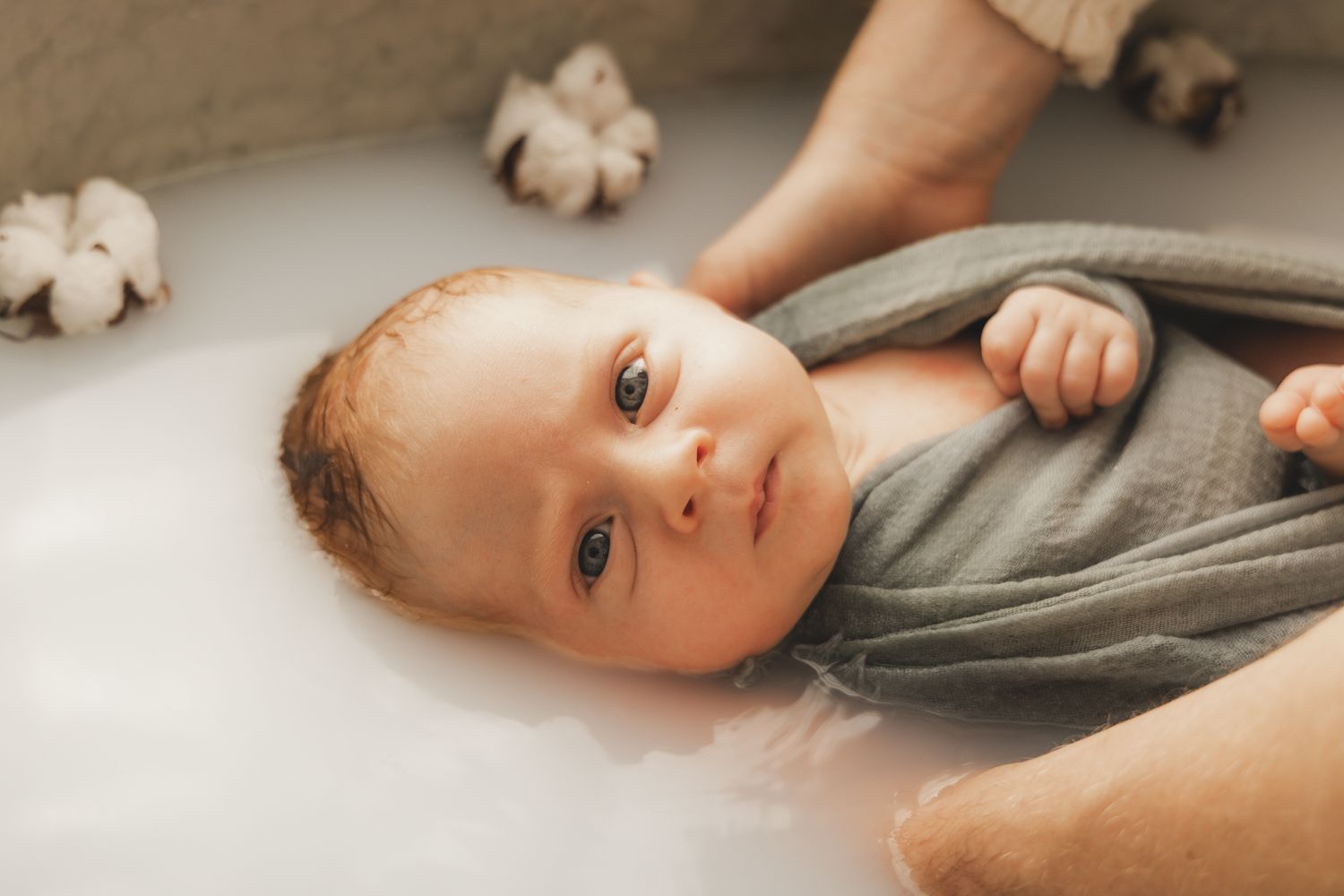 Alert newborn baby with wide eyes, wrapped in green cloth during a milk bath.