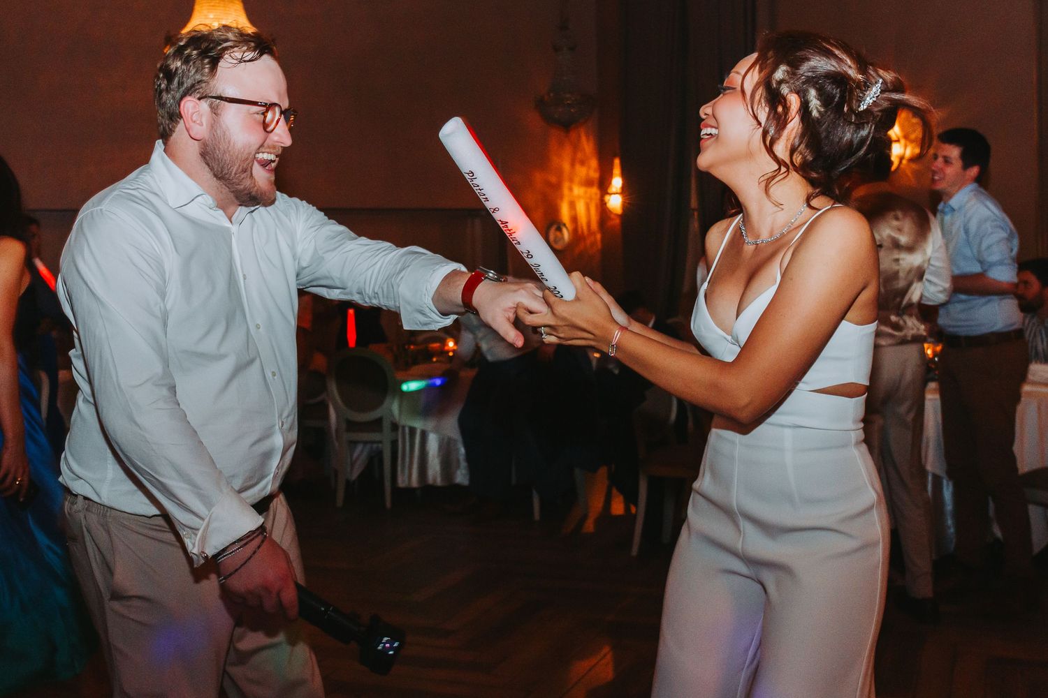Bride and groom laughing and playing with light sticks on the wedding reception dance floor.