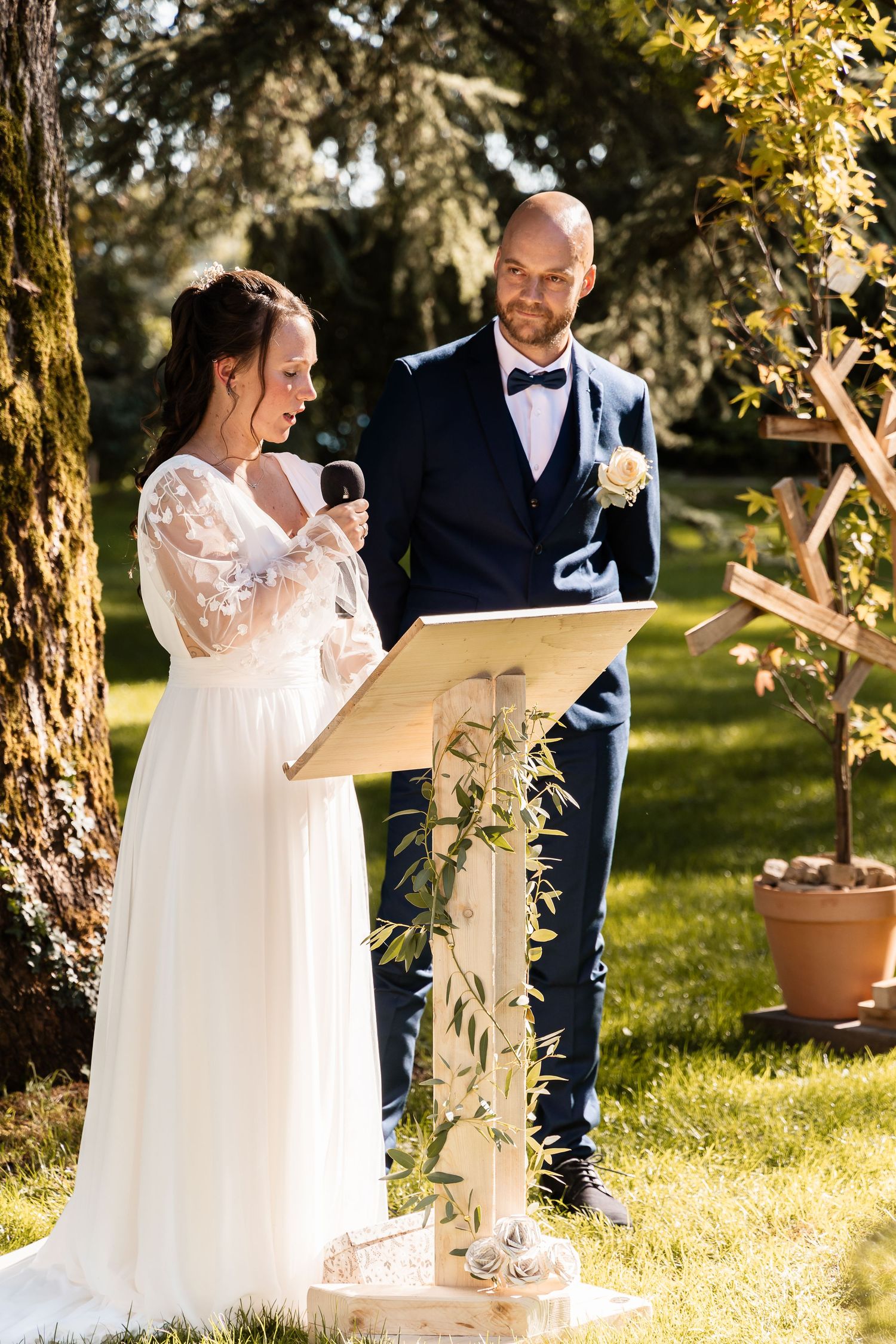 Bride reads her wedding vows at a decorated podium while groom watches lovingly during outdoor ceremony.